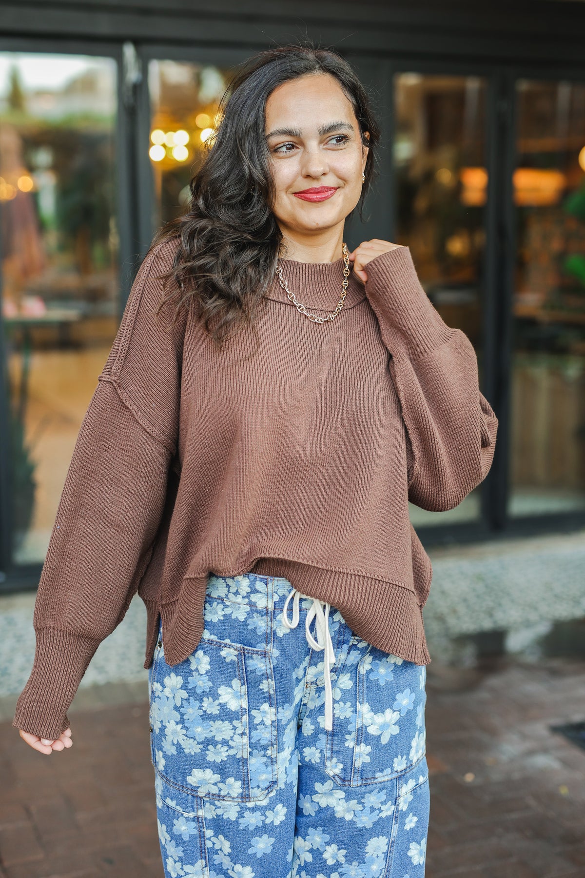 Woman wearing a brown sweater and blue floral pants standing outdoors.