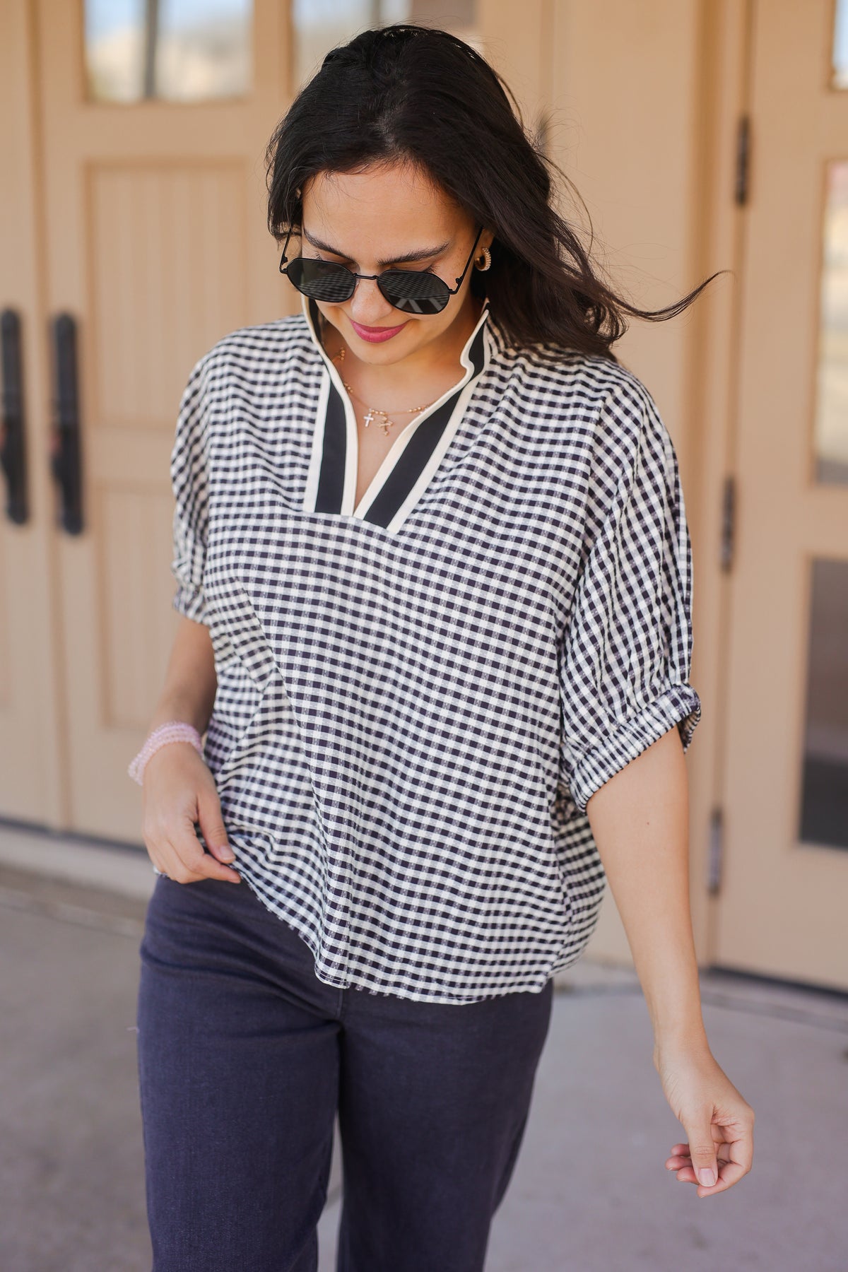 Woman wearing a black and white checkered shirt and sunglasses, standing in front of a building.