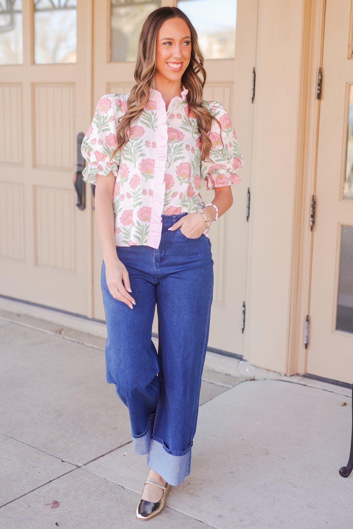 Woman wearing a floral blouse and blue jeans standing in front of a beige door.