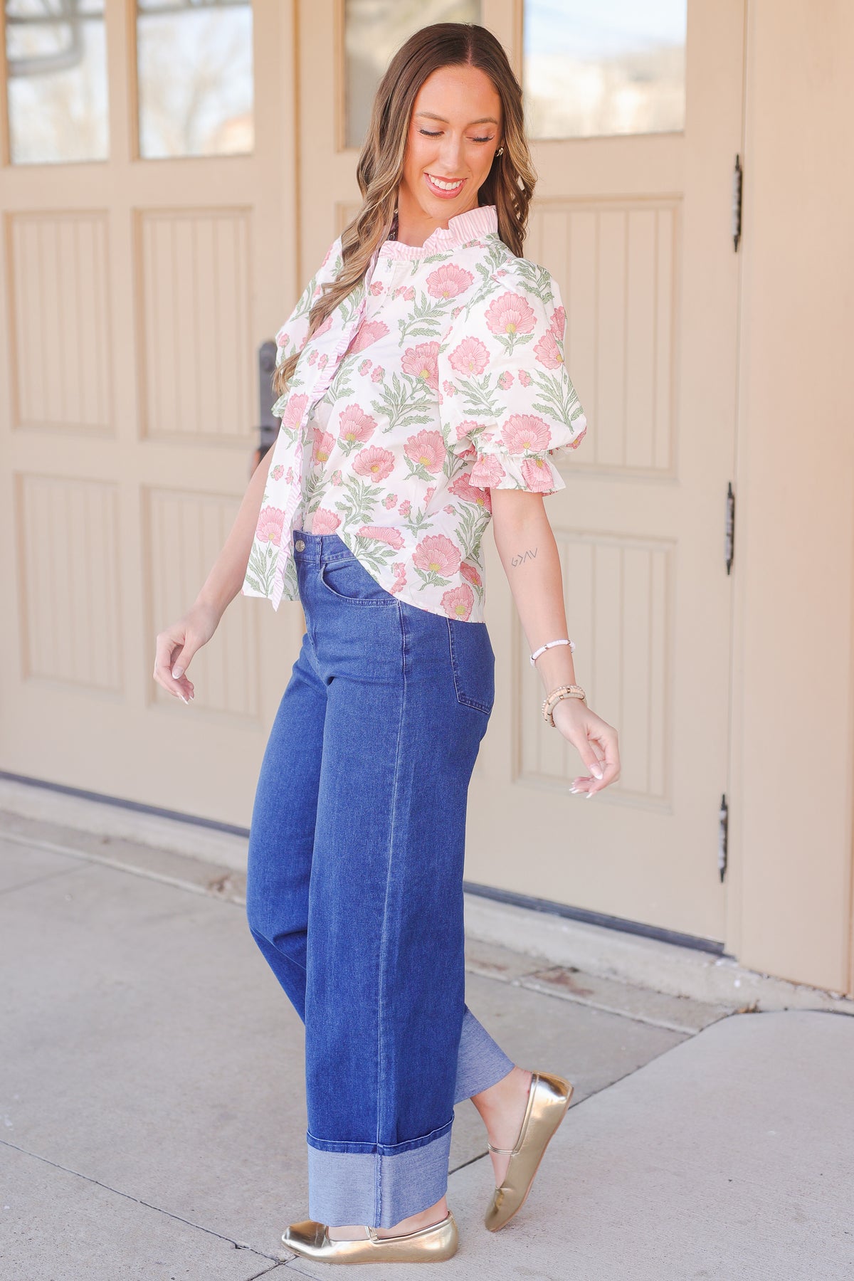 Woman wearing a floral blouse and blue jeans standing in front of a beige door.