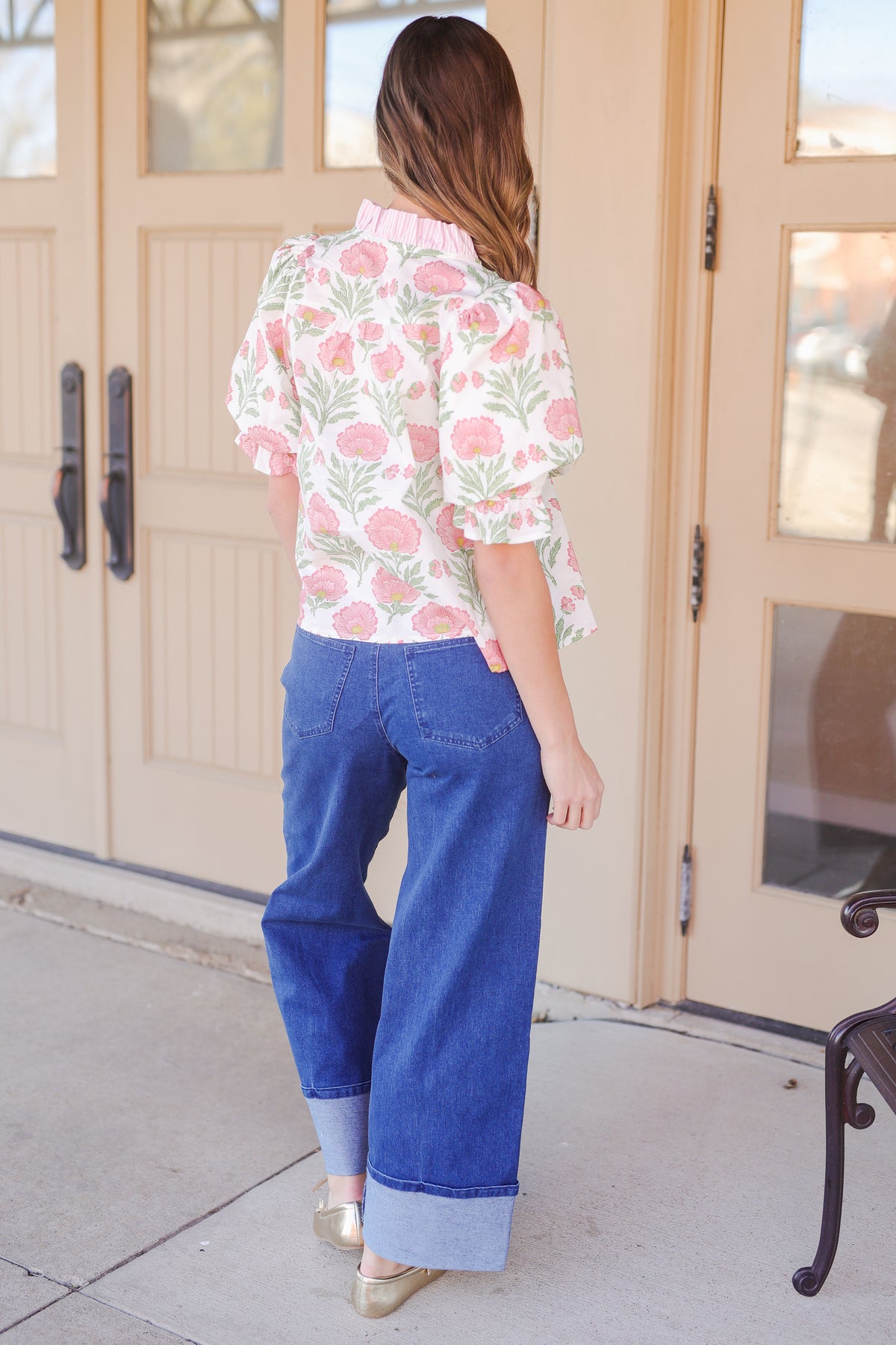 Woman wearing a floral blouse and blue jeans standing in front of glass doors.