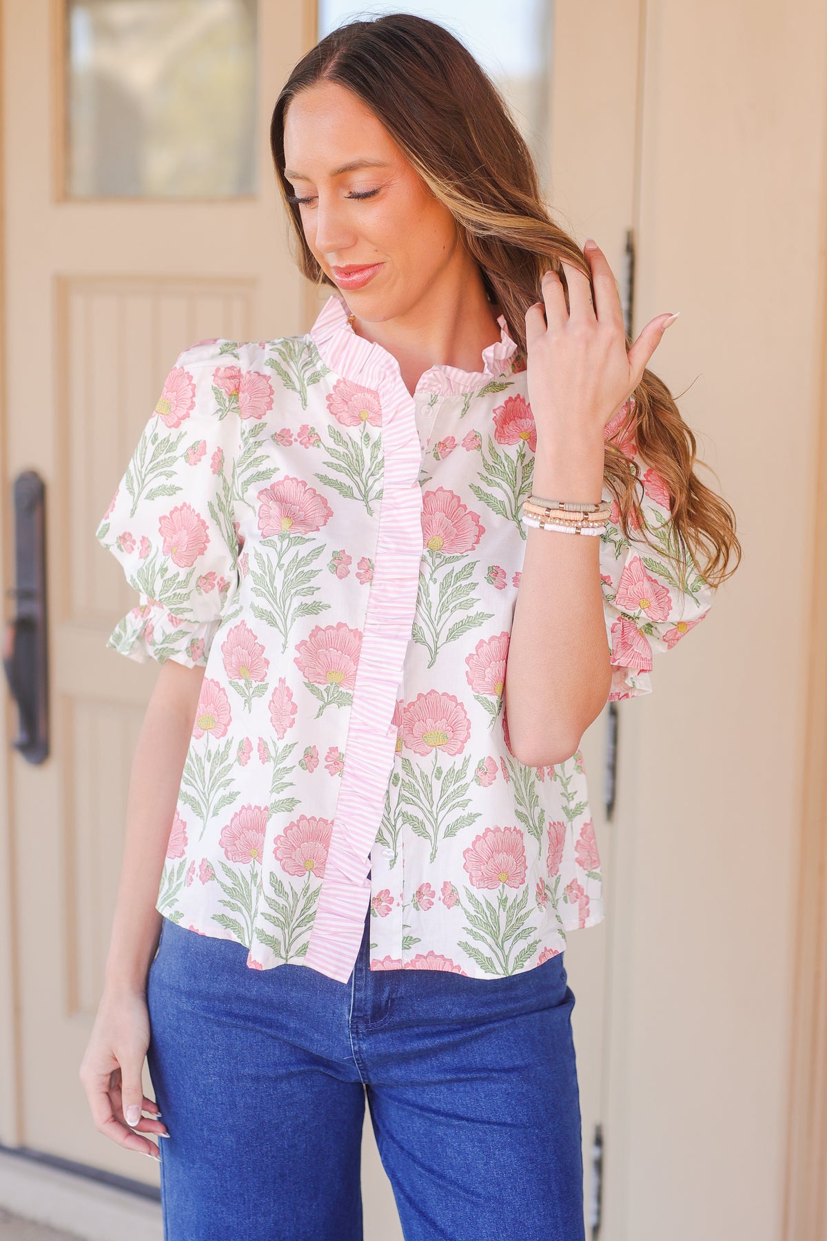 Woman wearing a floral blouse with pink flowers and green leaves, standing in front of a door.