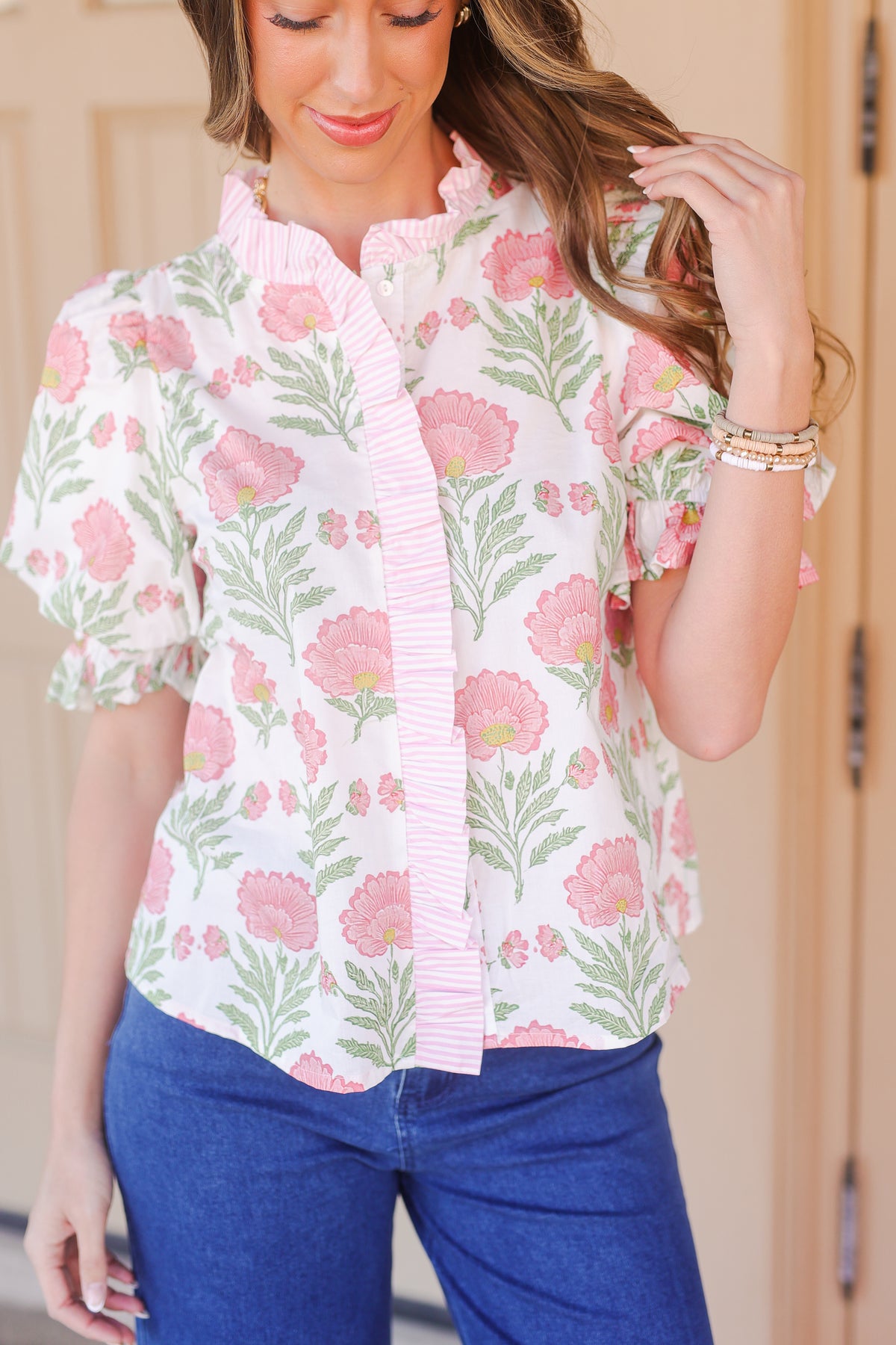 Woman wearing a floral blouse with pink flowers and green leaves, standing against a neutral background.