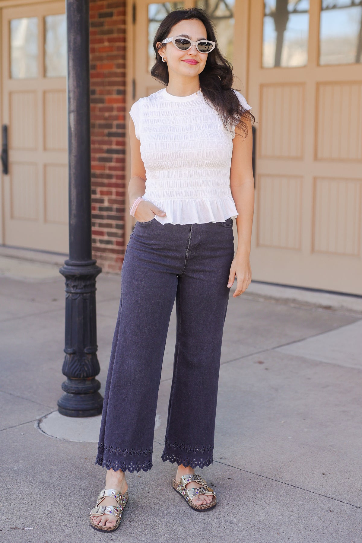 Woman wearing a white top and dark blue jeans standing on a sidewalk.