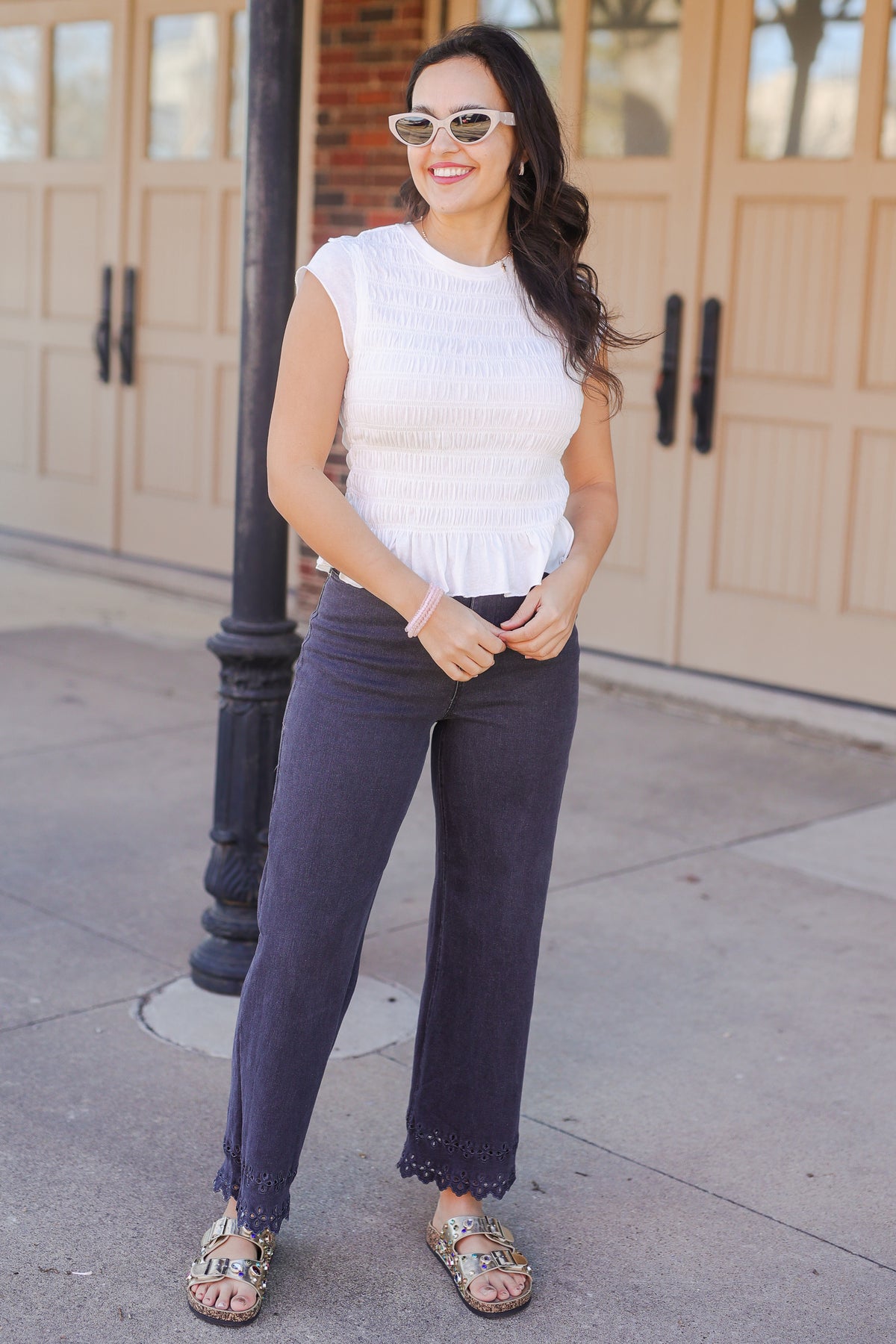 Woman wearing a white top and dark pants standing on a sidewalk.