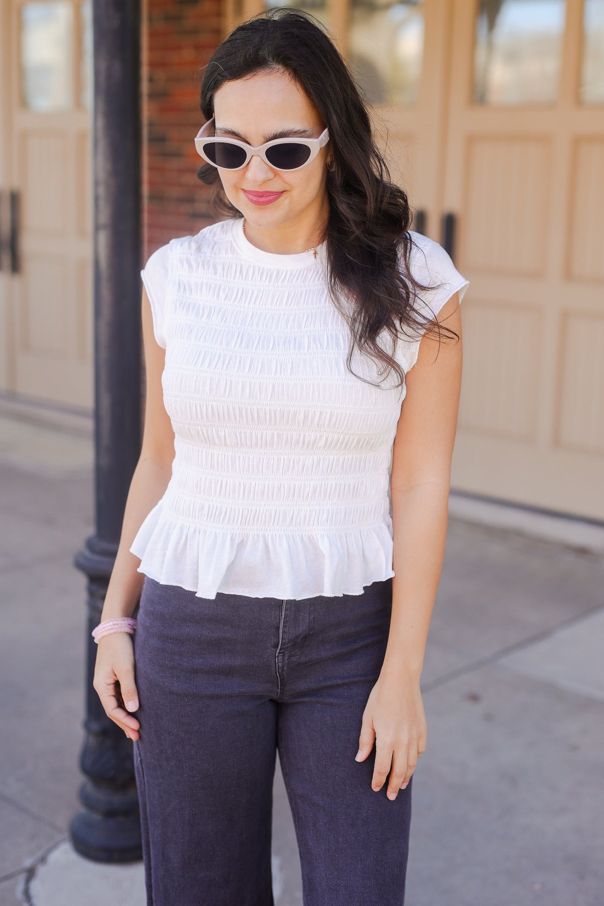 Woman wearing a white peplum top and dark pants outdoors.