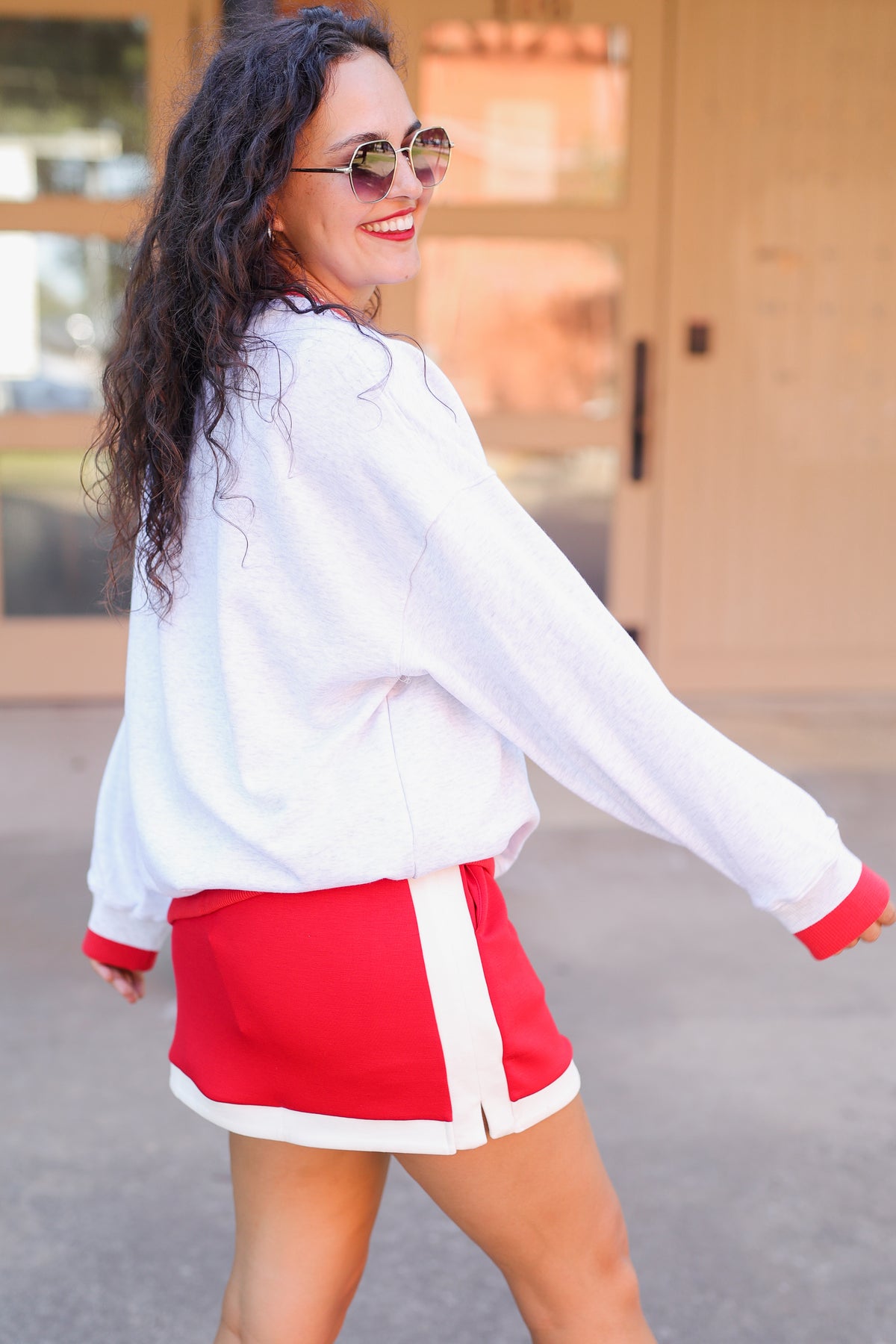 Woman wearing a white long-sleeve shirt and red shorts with white trim, standing outdoors.
