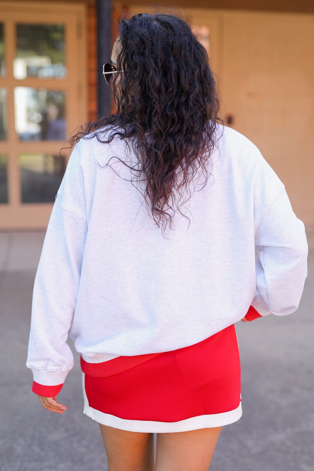 Person wearing a white sweatshirt and red skirt with a neutral background