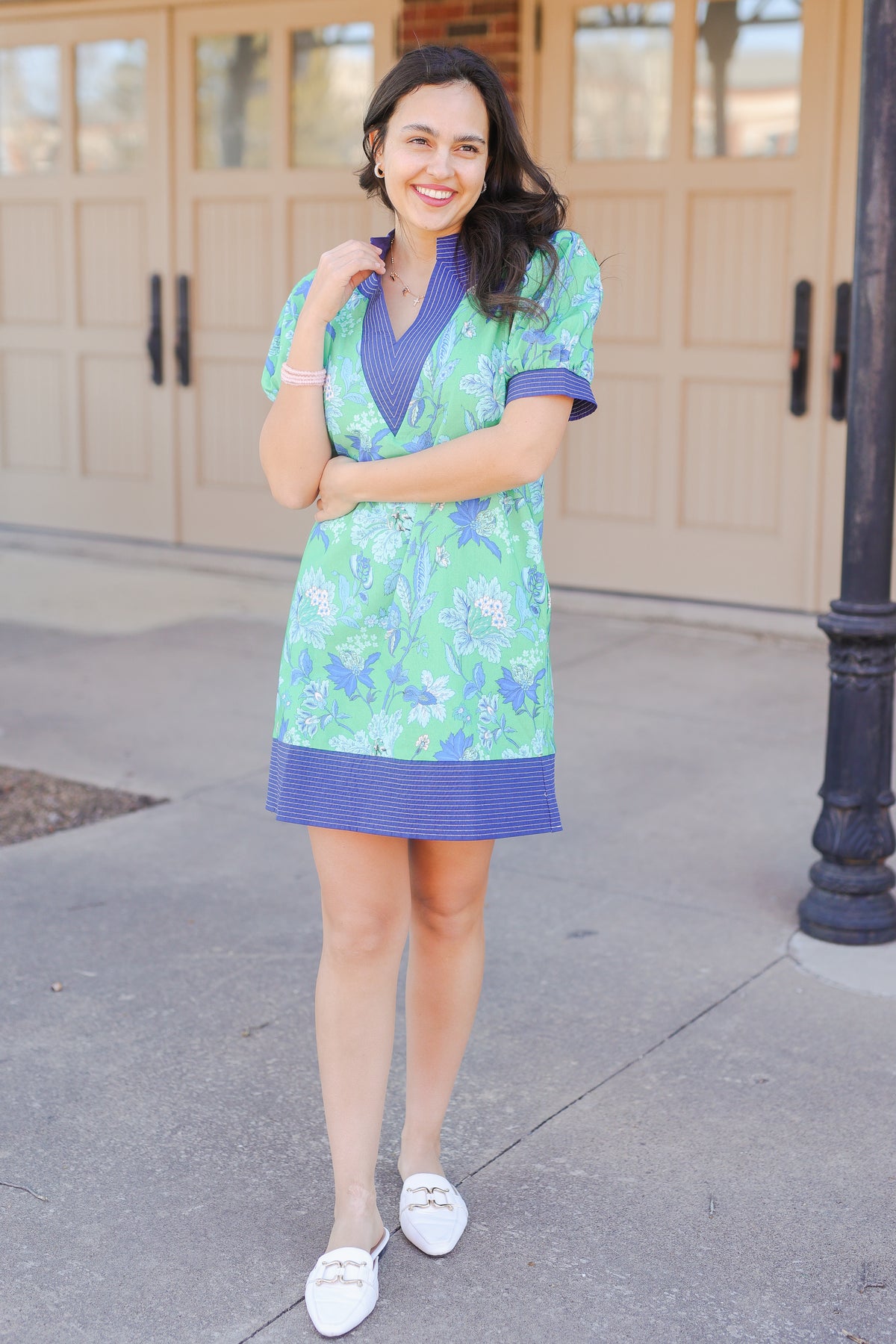 Woman wearing a green and blue floral dress standing on a sidewalk.