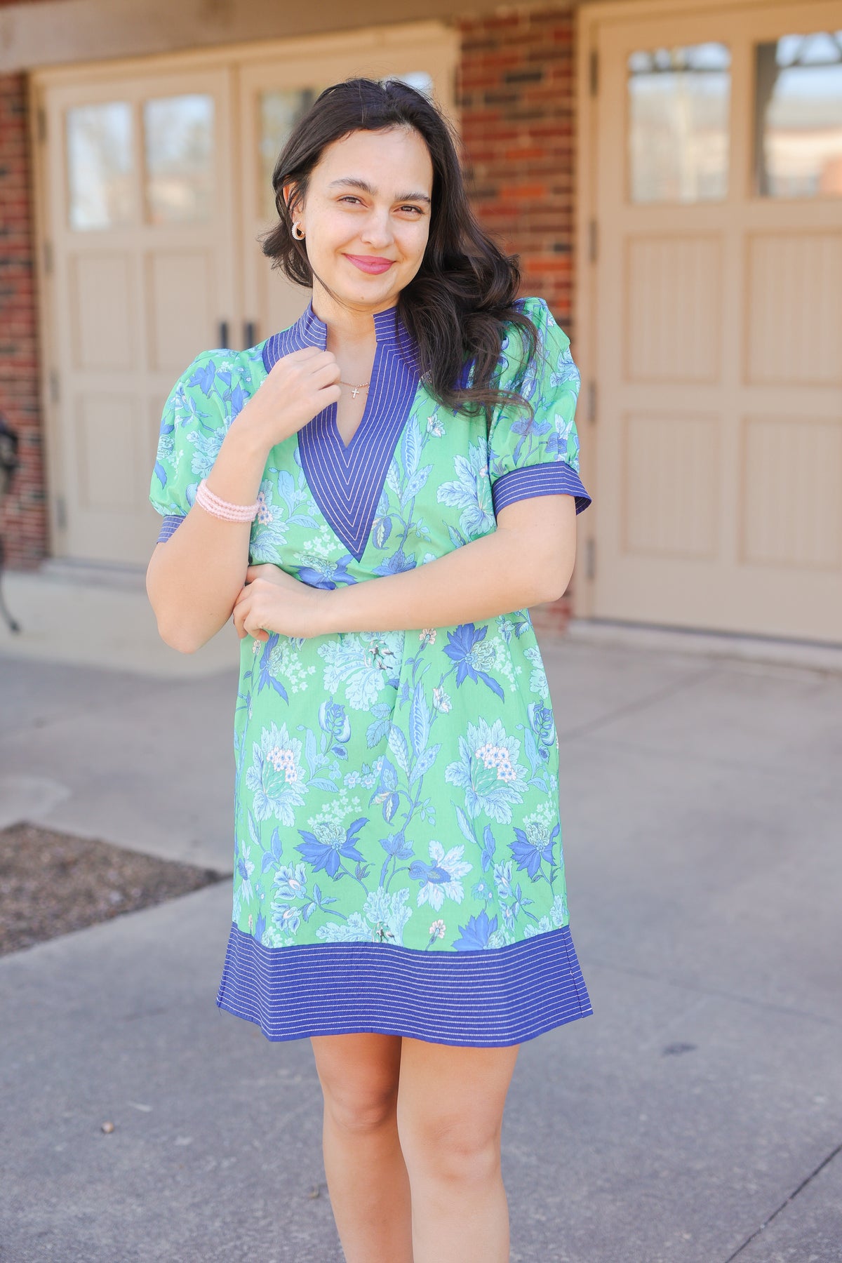 Woman wearing a green floral dress with blue accents standing outside a building.