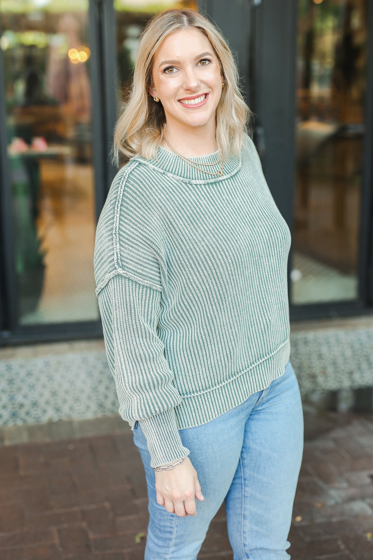 Woman wearing a green sweater and blue jeans standing outdoors.