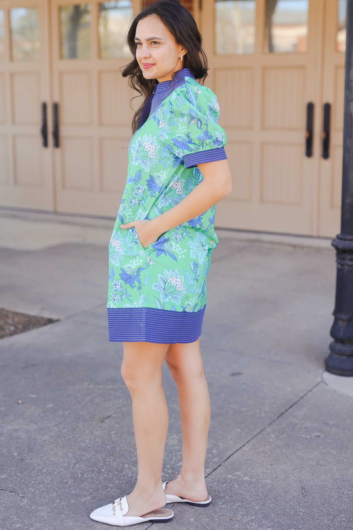Woman wearing a green and blue dress with floral pattern standing on a sidewalk.