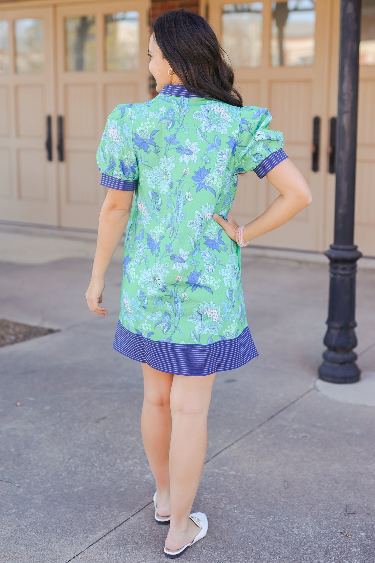 Woman wearing a green floral dress with blue accents on a sidewalk.