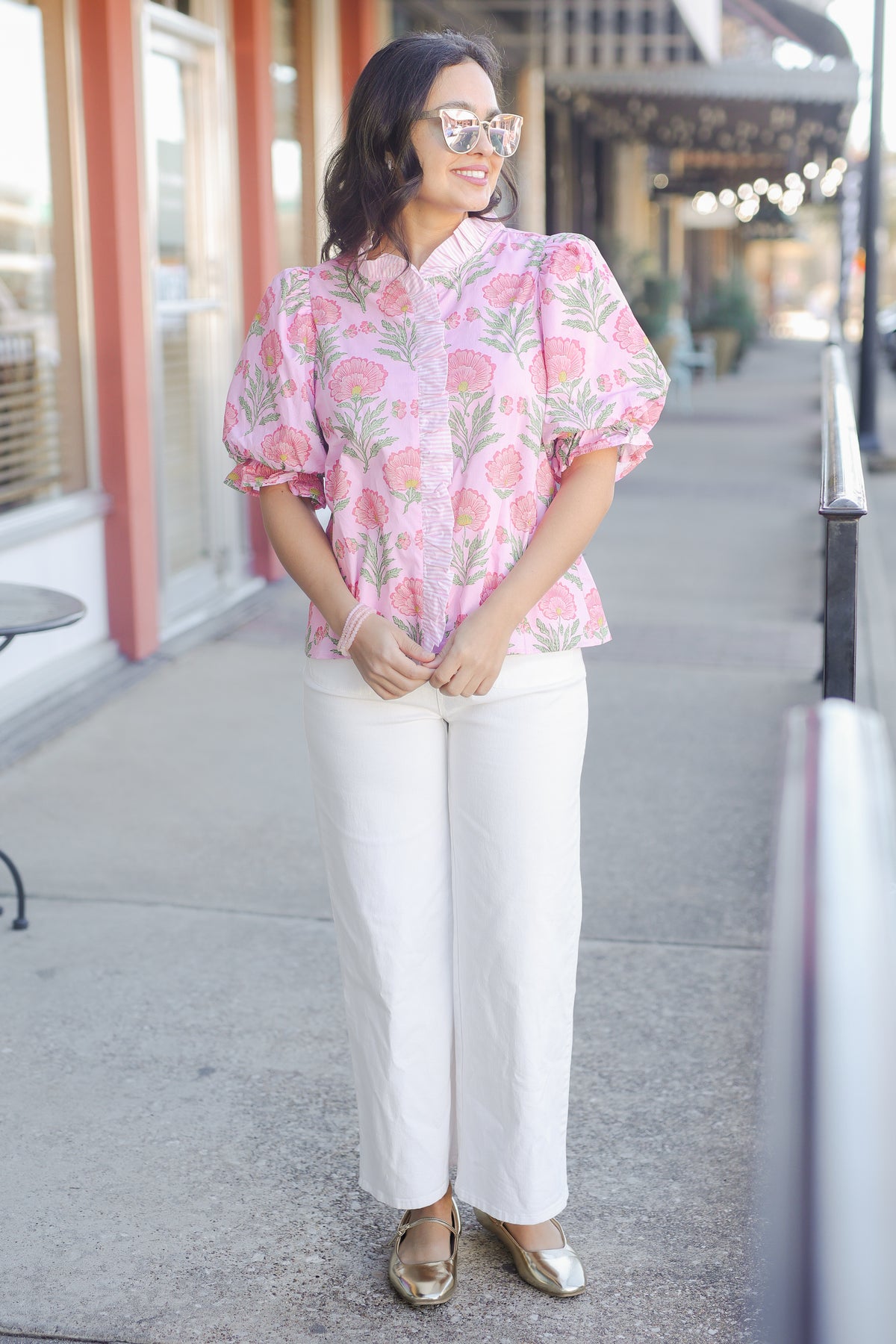 Woman wearing a pink floral blouse and white pants on a city street.