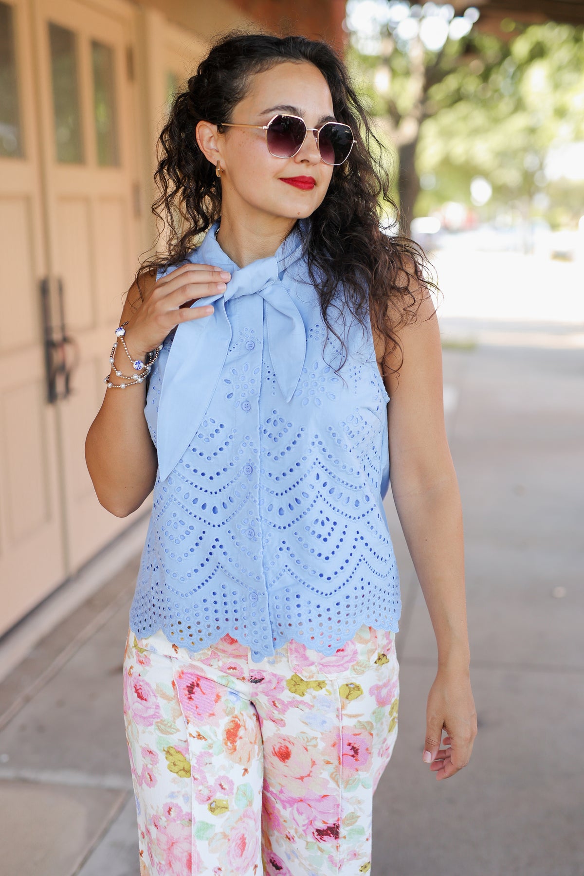 Woman wearing a light blue sleeveless top with a bow and floral pants outdoors.
