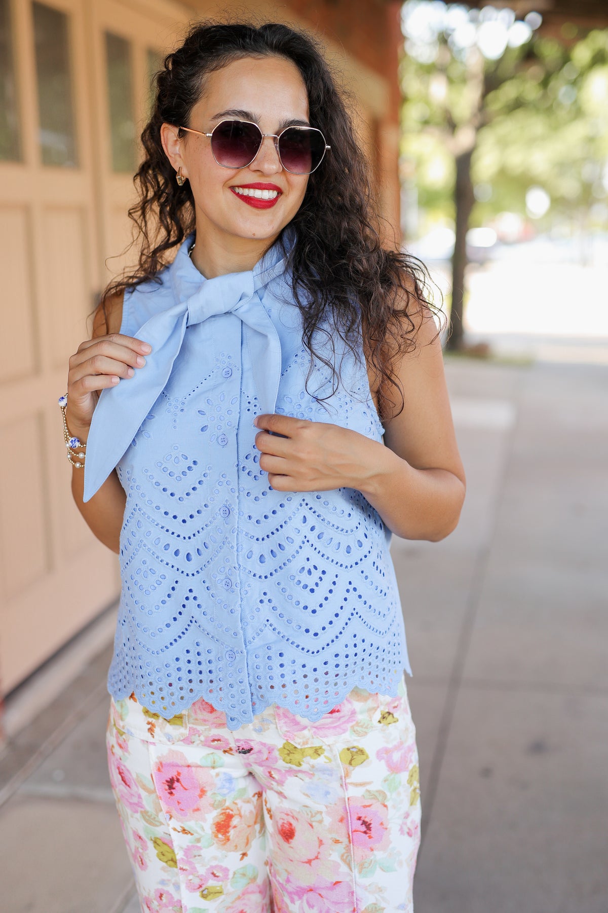 Woman wearing a light blue sleeveless top with a bow and floral pants outdoors.
