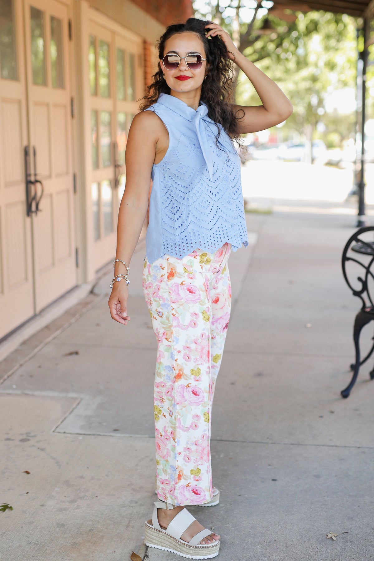Woman wearing a light blue sleeveless top and floral pants on a sidewalk.
