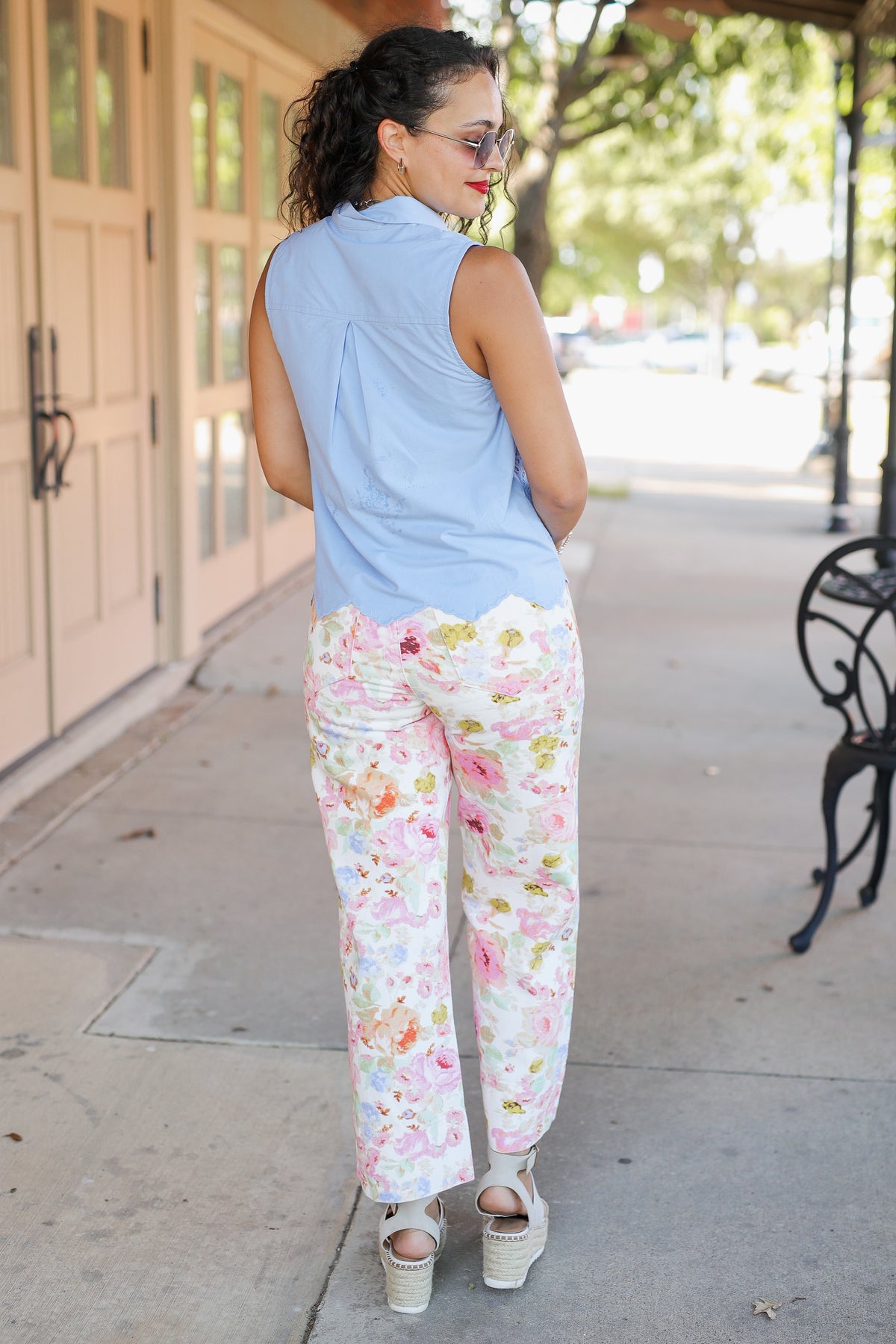 Woman wearing a light blue sleeveless top and floral pants on a sidewalk.
