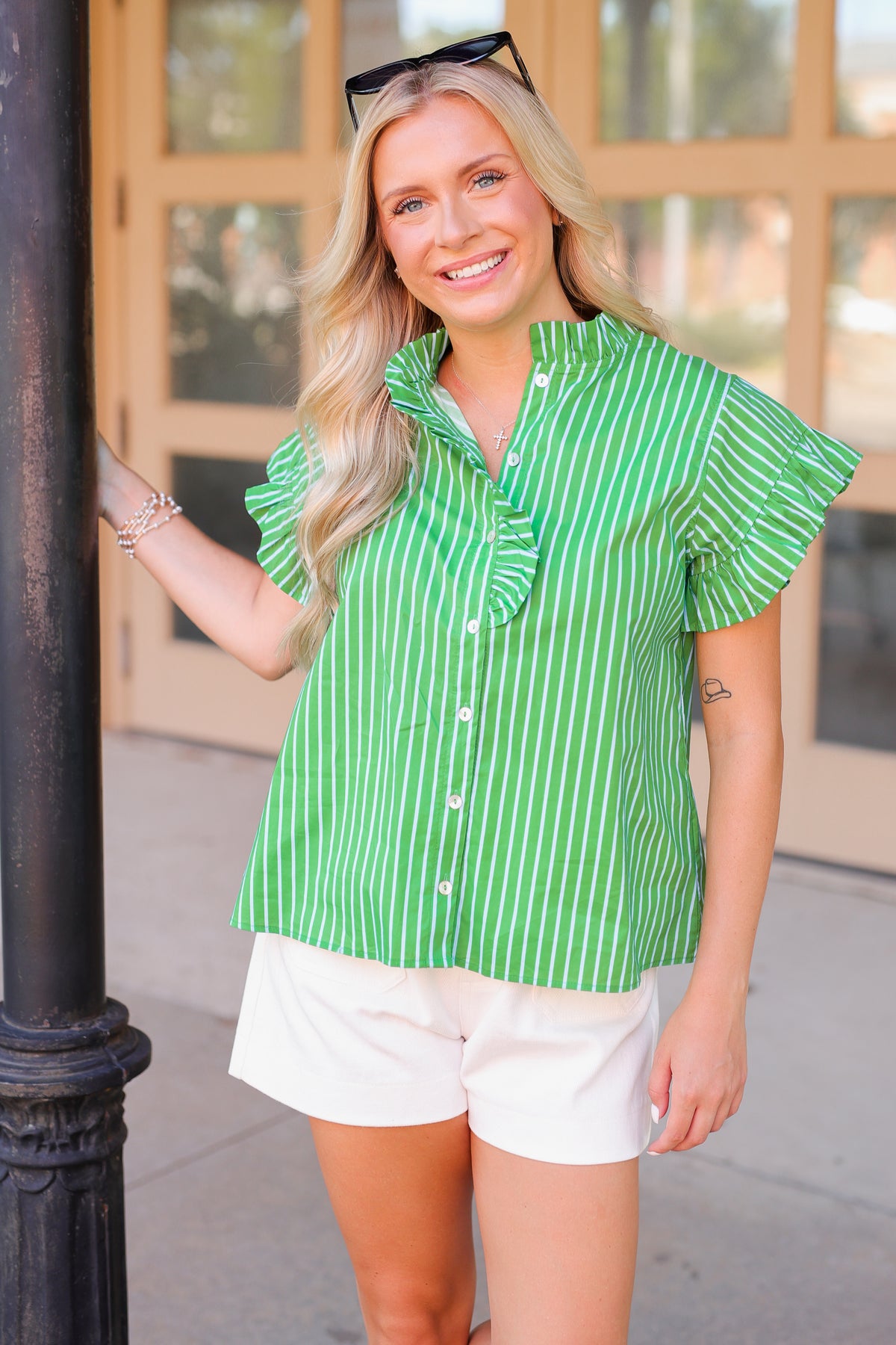 Woman wearing a green and white striped shirt and white shorts standing outdoors.