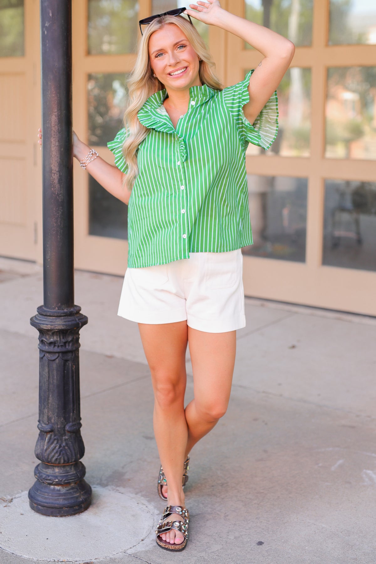 Woman in a green striped shirt and white shorts standing next to a black pole.