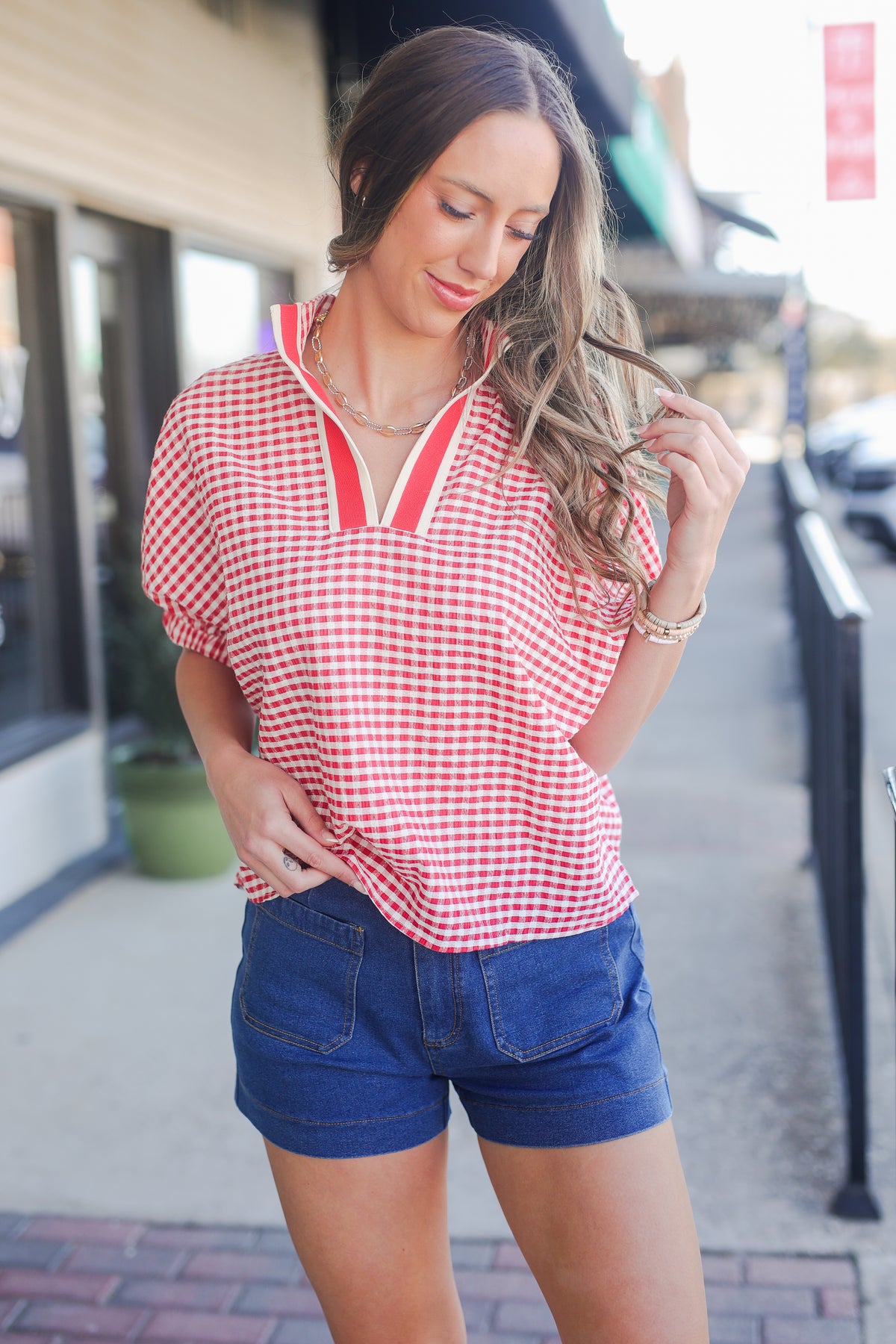 Woman wearing a red and white checkered shirt and blue shorts on a city street.