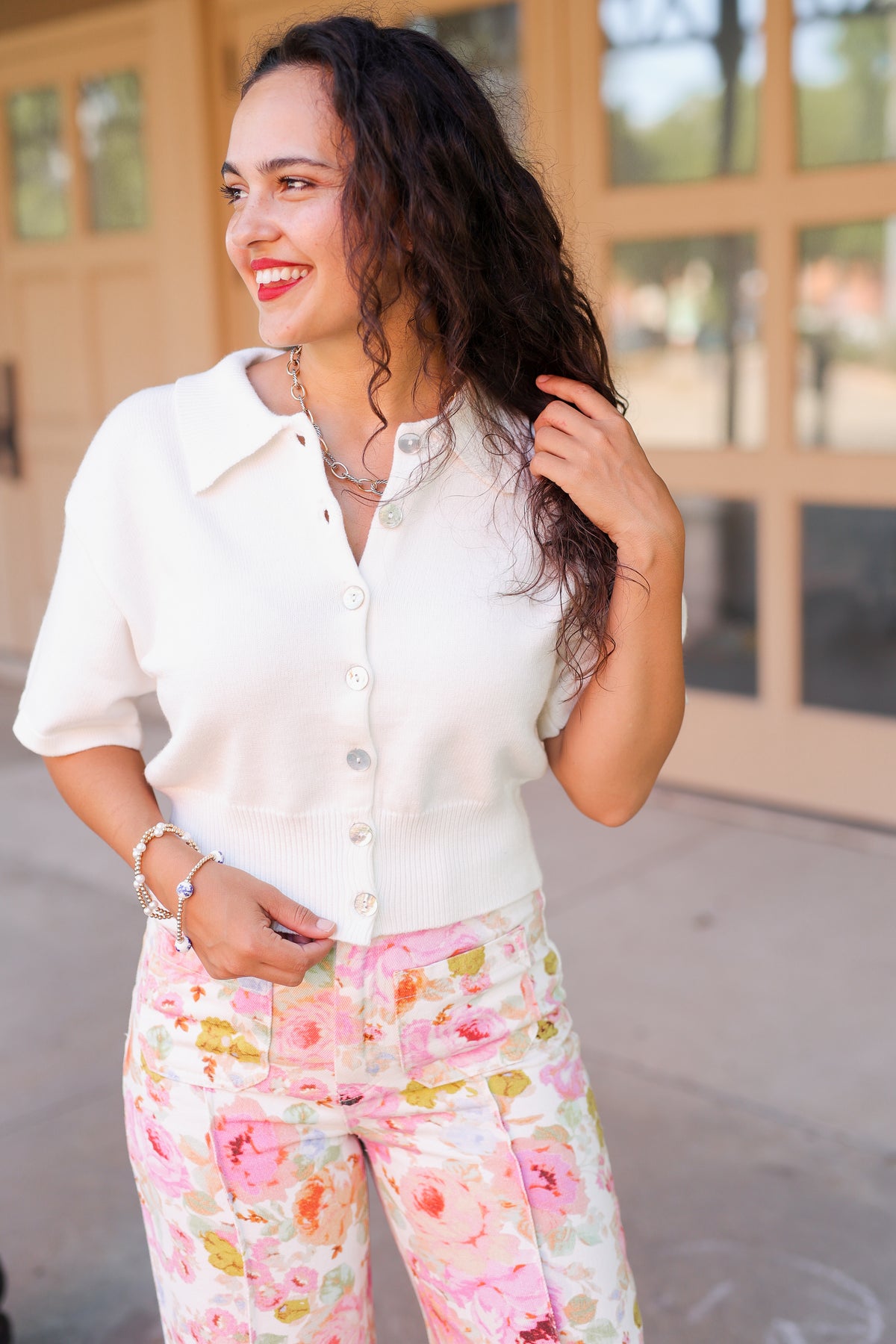 Brunette model standing outside wearing a off white cardigan and floral pattern denim pants.