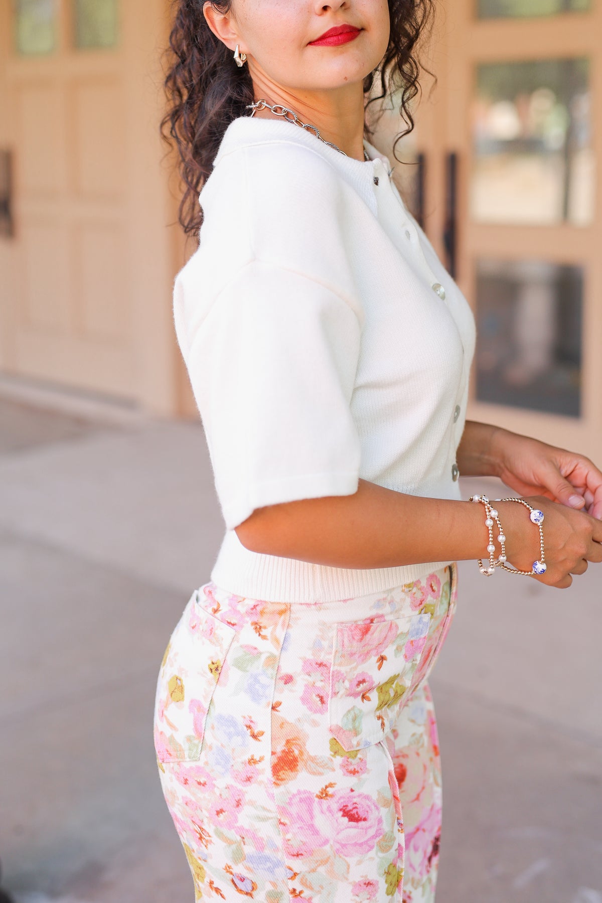 Brunette model standing outside wearing a off white cardigan and floral pattern denim pants.