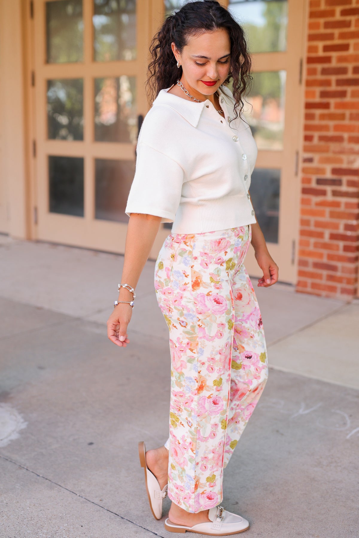 Brunette model standing outside wearing a off white cardigan and floral pattern denim pants.