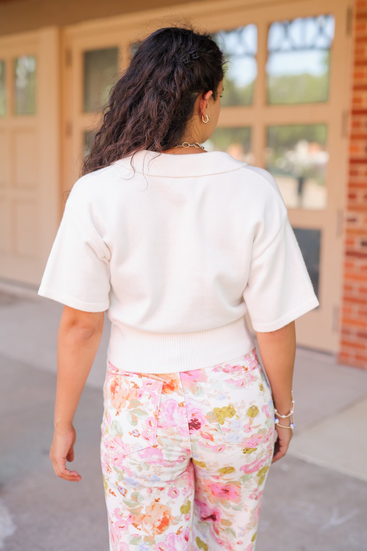 Brunette model standing outside wearing a off white cardigan and floral pattern denim pants.