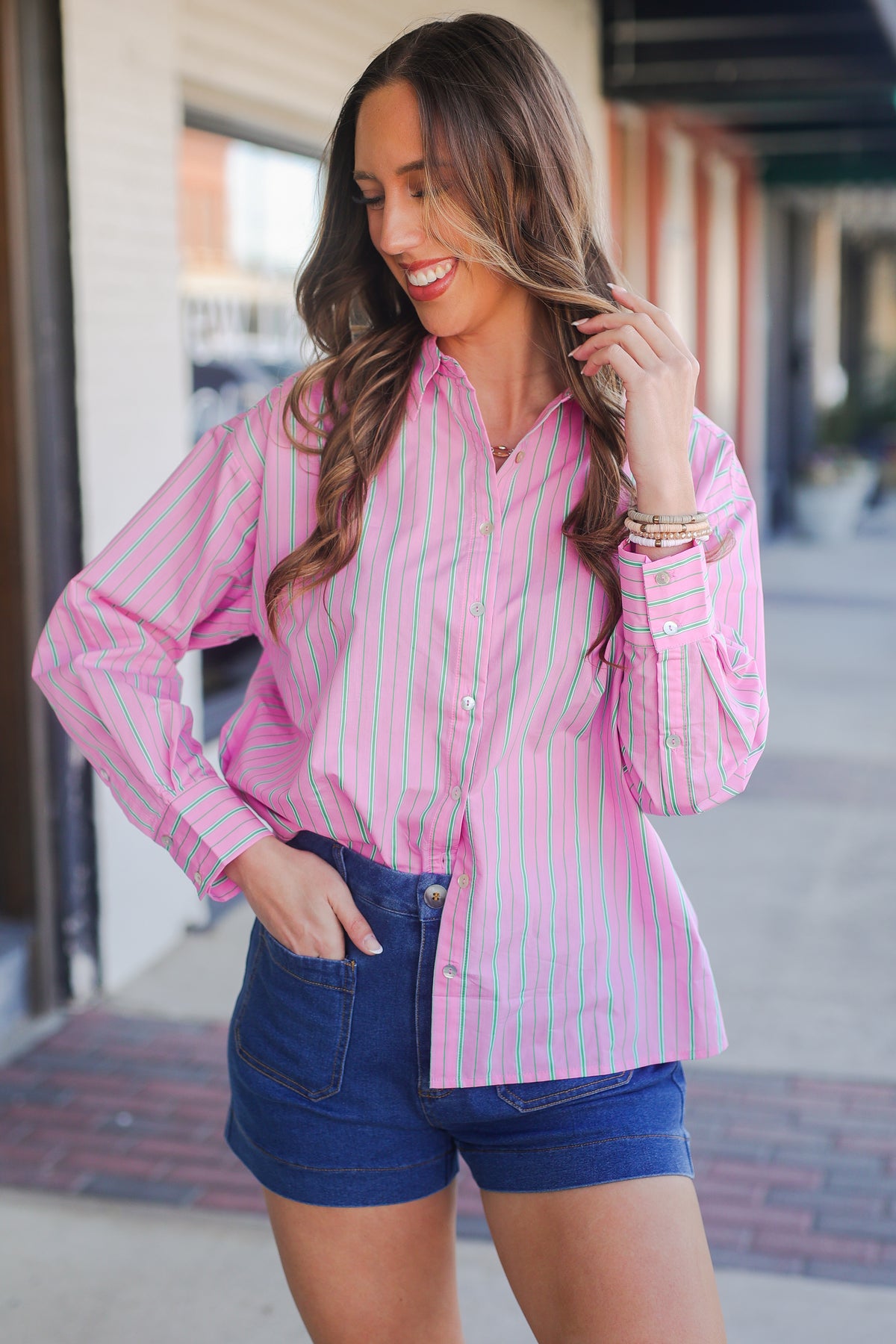 Woman wearing a pink striped shirt and blue shorts standing outdoors.