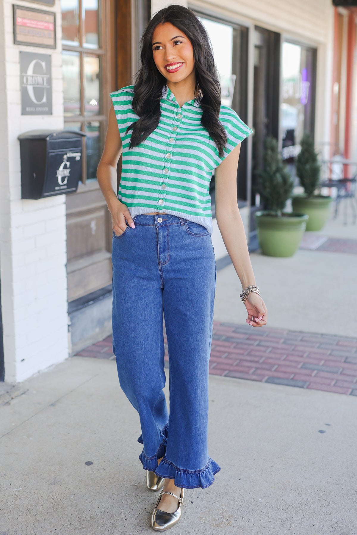 Woman wearing a green and white striped shirt and blue jeans on a sidewalk.