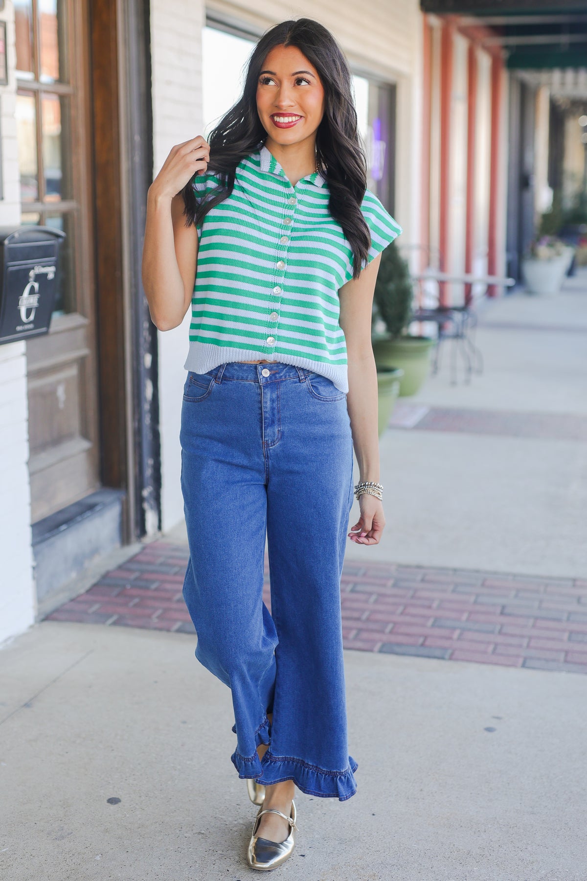 Woman wearing a green and white striped shirt and blue jeans on a sidewalk.