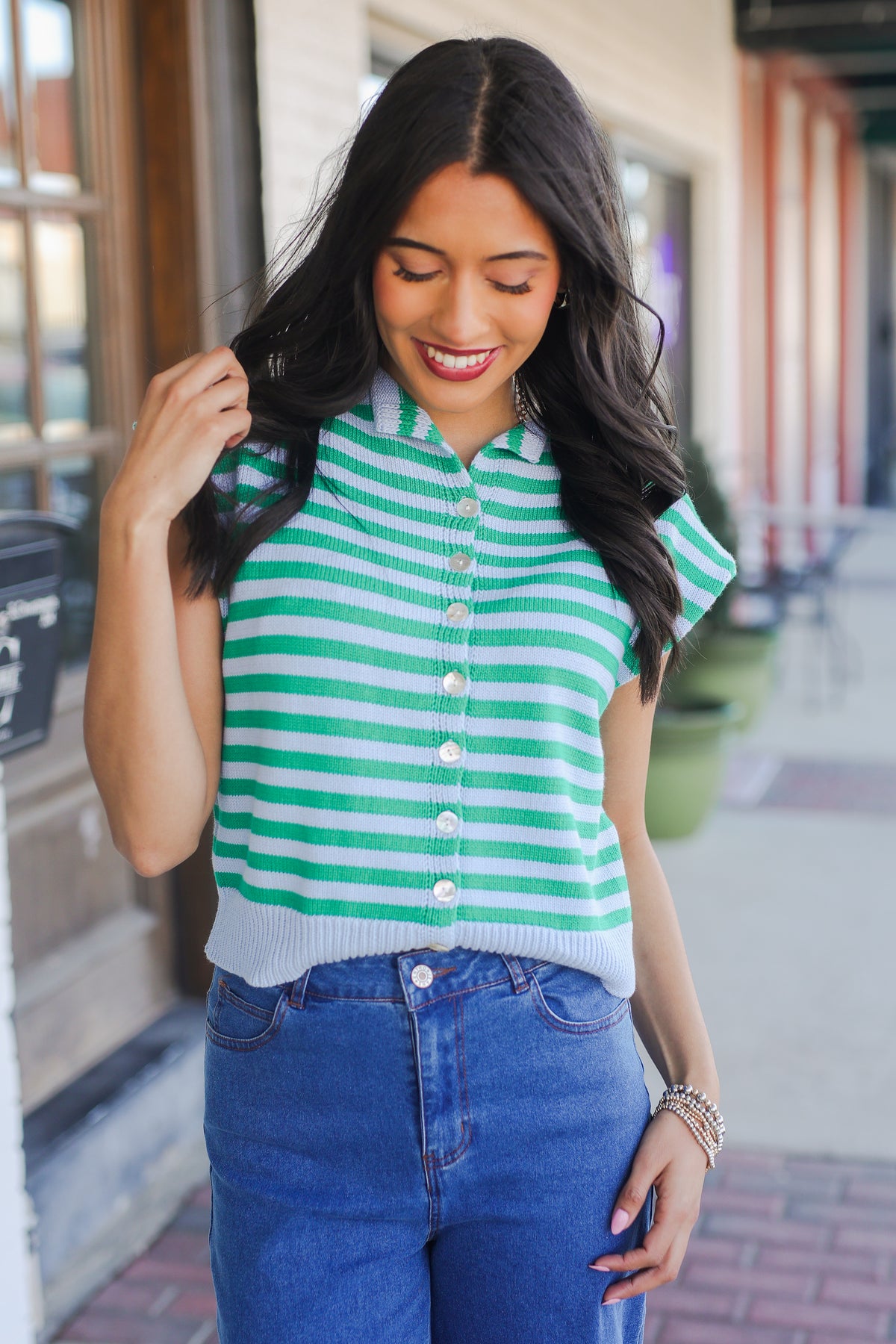 Woman wearing a green and white striped shirt and blue jeans outdoors.