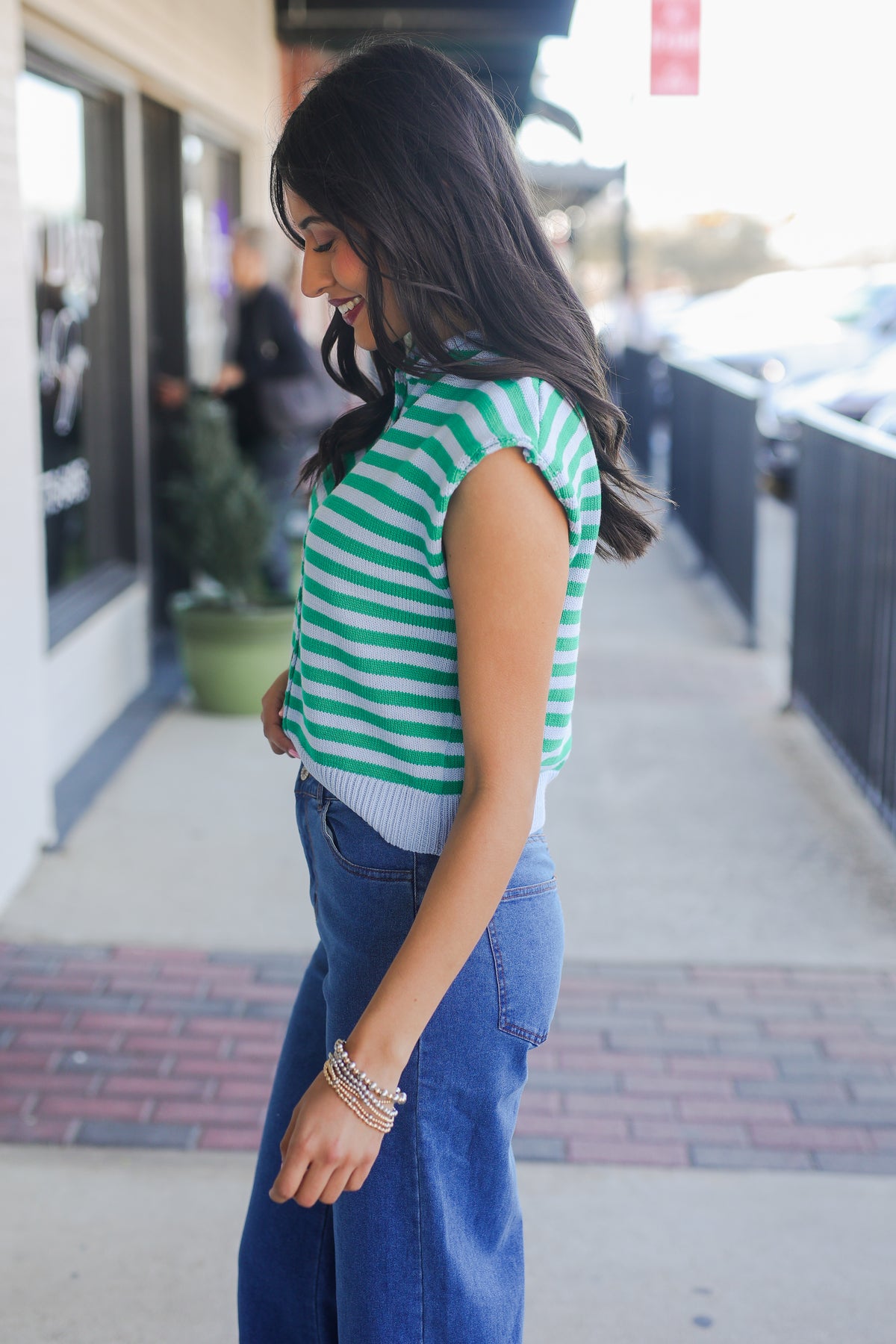 Woman wearing a green and white striped shirt and blue jeans in an urban setting.
