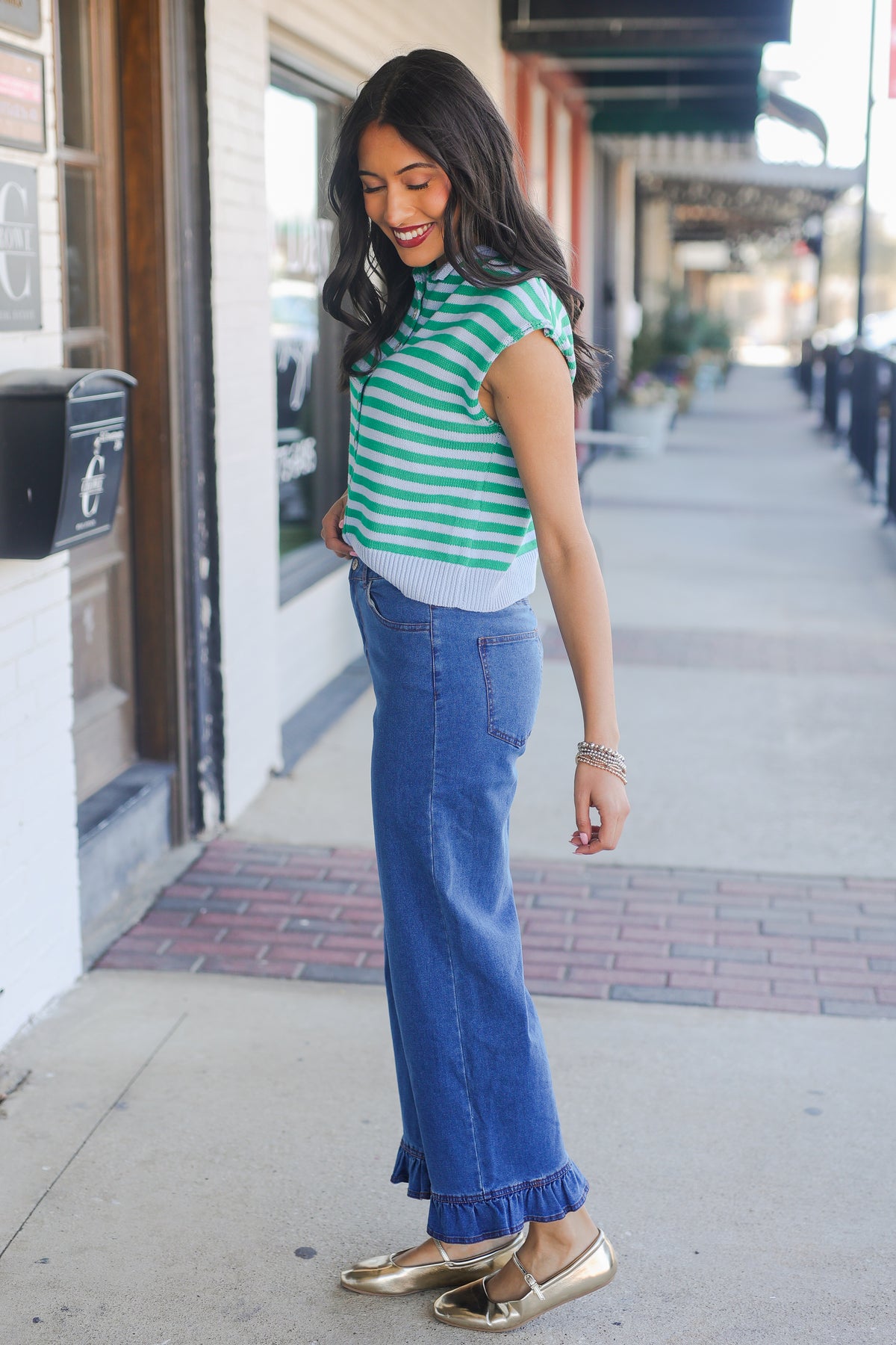 Woman wearing a green and white striped shirt and blue jeans on a sidewalk.