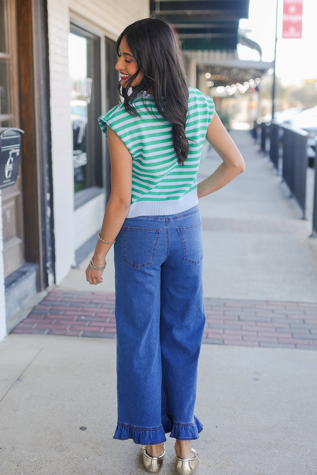Woman wearing a green and white striped shirt and blue jeans on a city street.