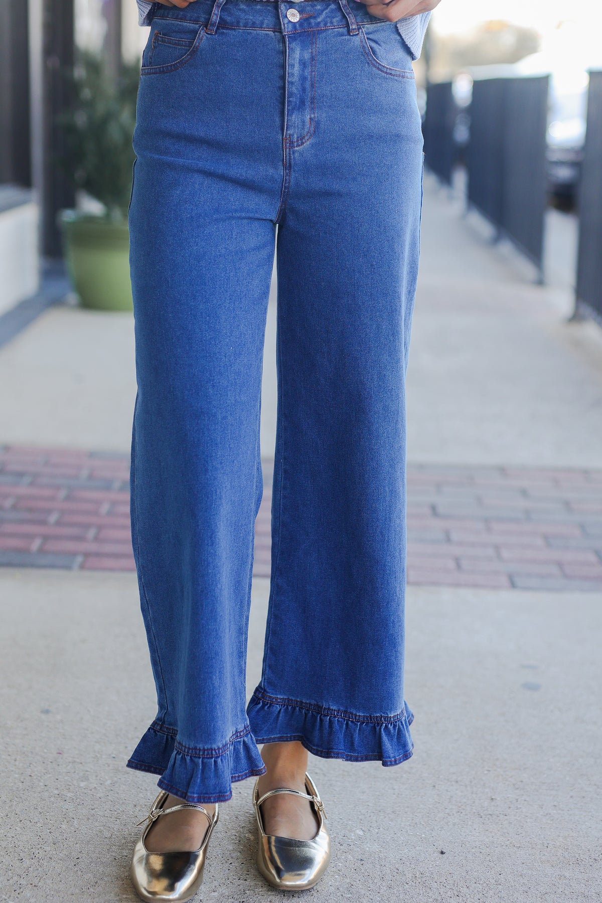 Person wearing blue jeans with ruffled cuffs on a sidewalk.