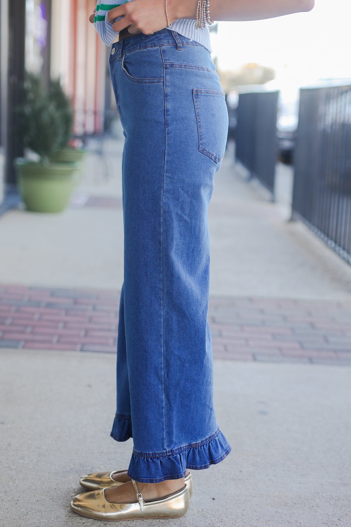 Person wearing blue jeans with ruffled hem on a sidewalk.