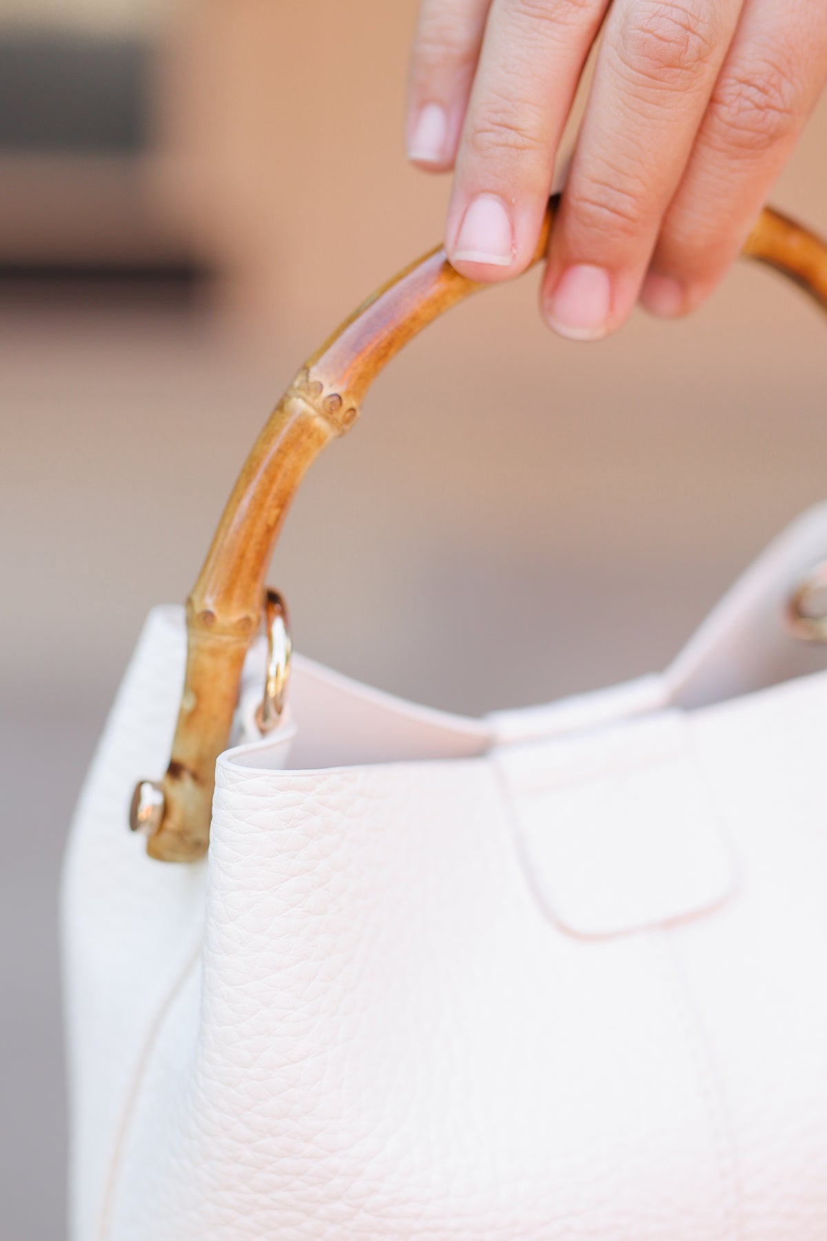 Woman holding a off white bucket bag with a bamboo handle.