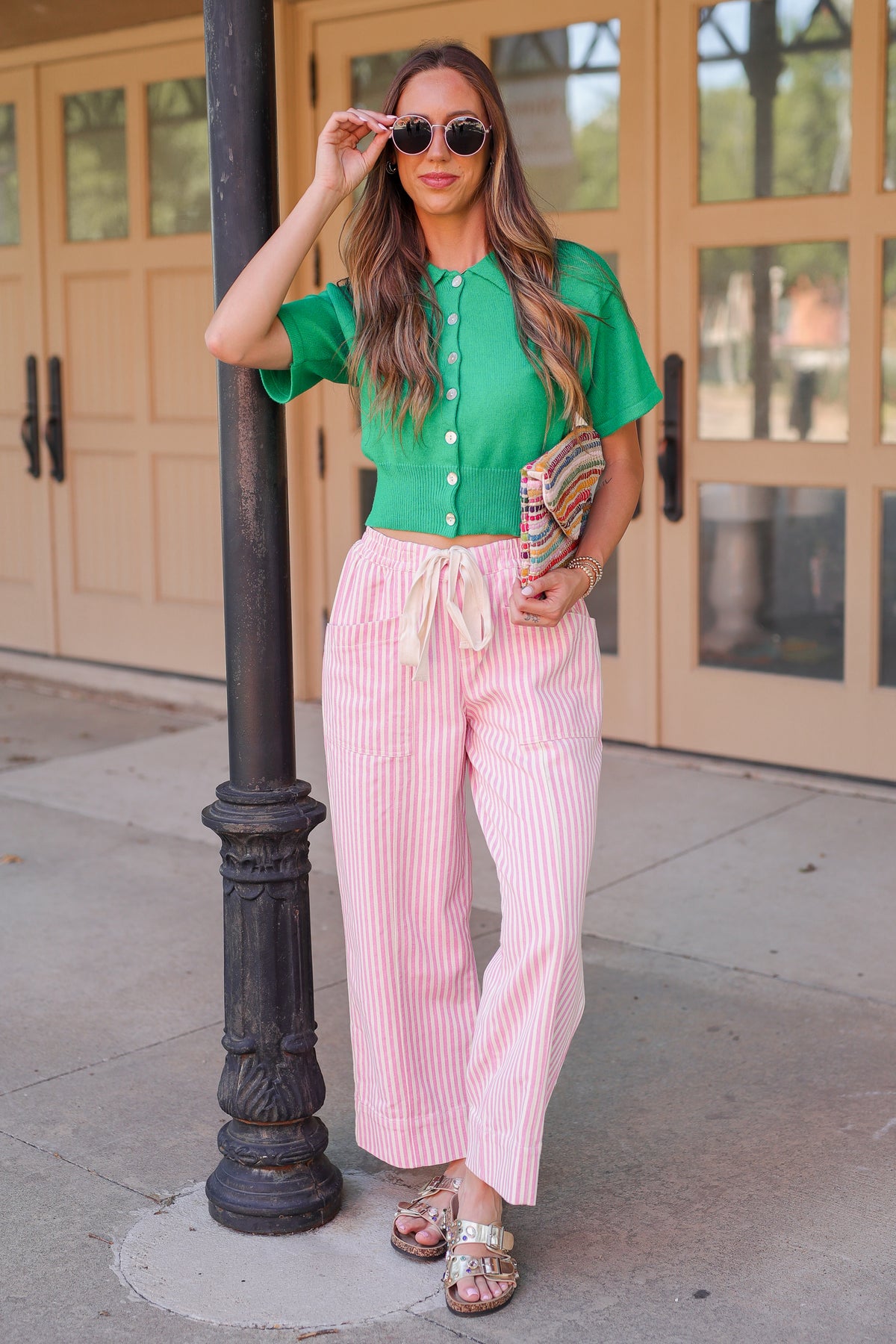 Woman in green top and pink striped pants standing on a sidewalk.