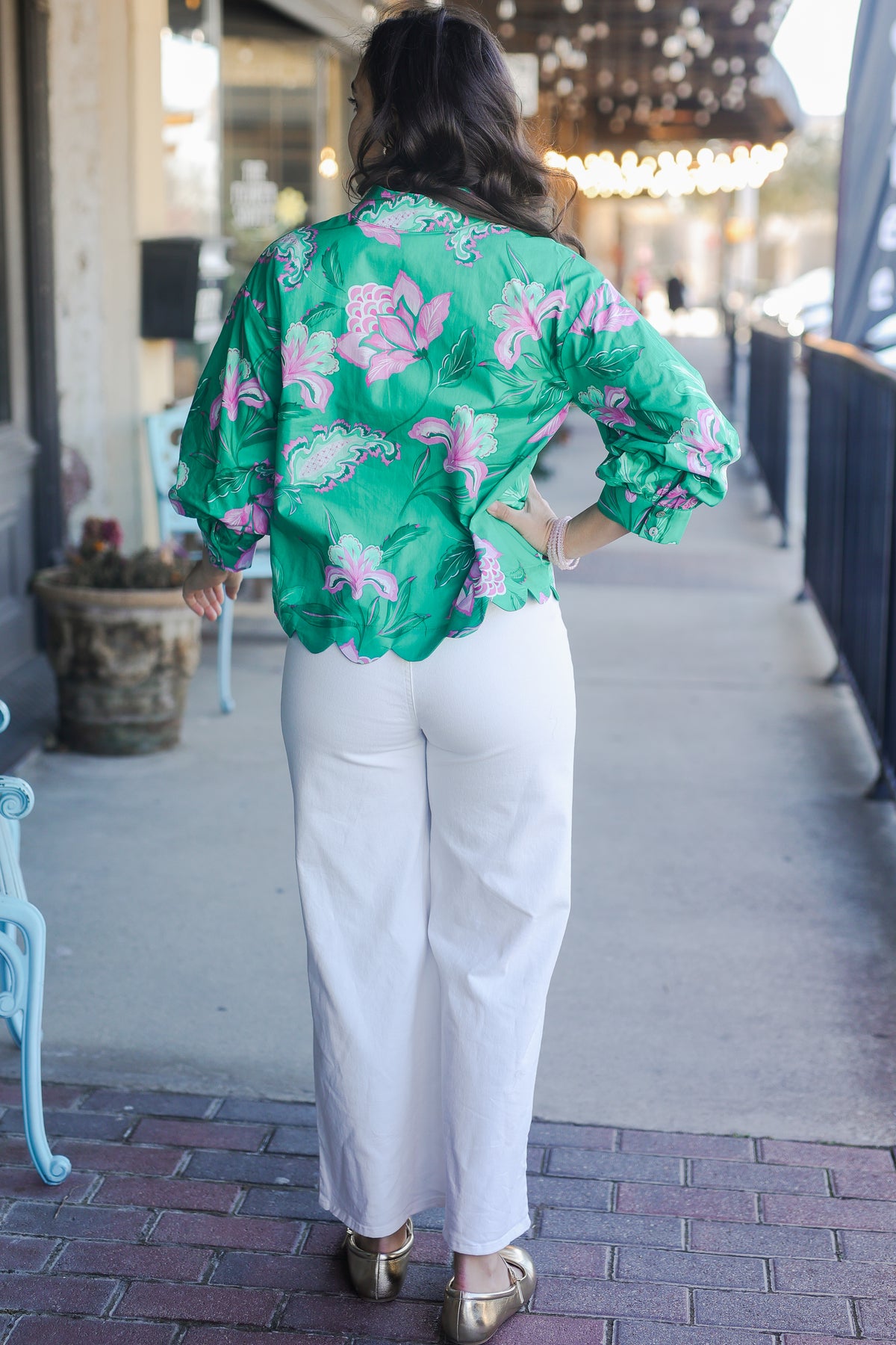 Woman wearing a green floral blouse and white pants walking on a sidewalk.