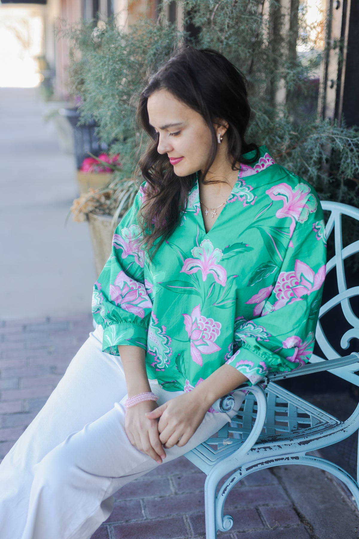 Woman in a green floral blouse sitting on a bench outdoors.