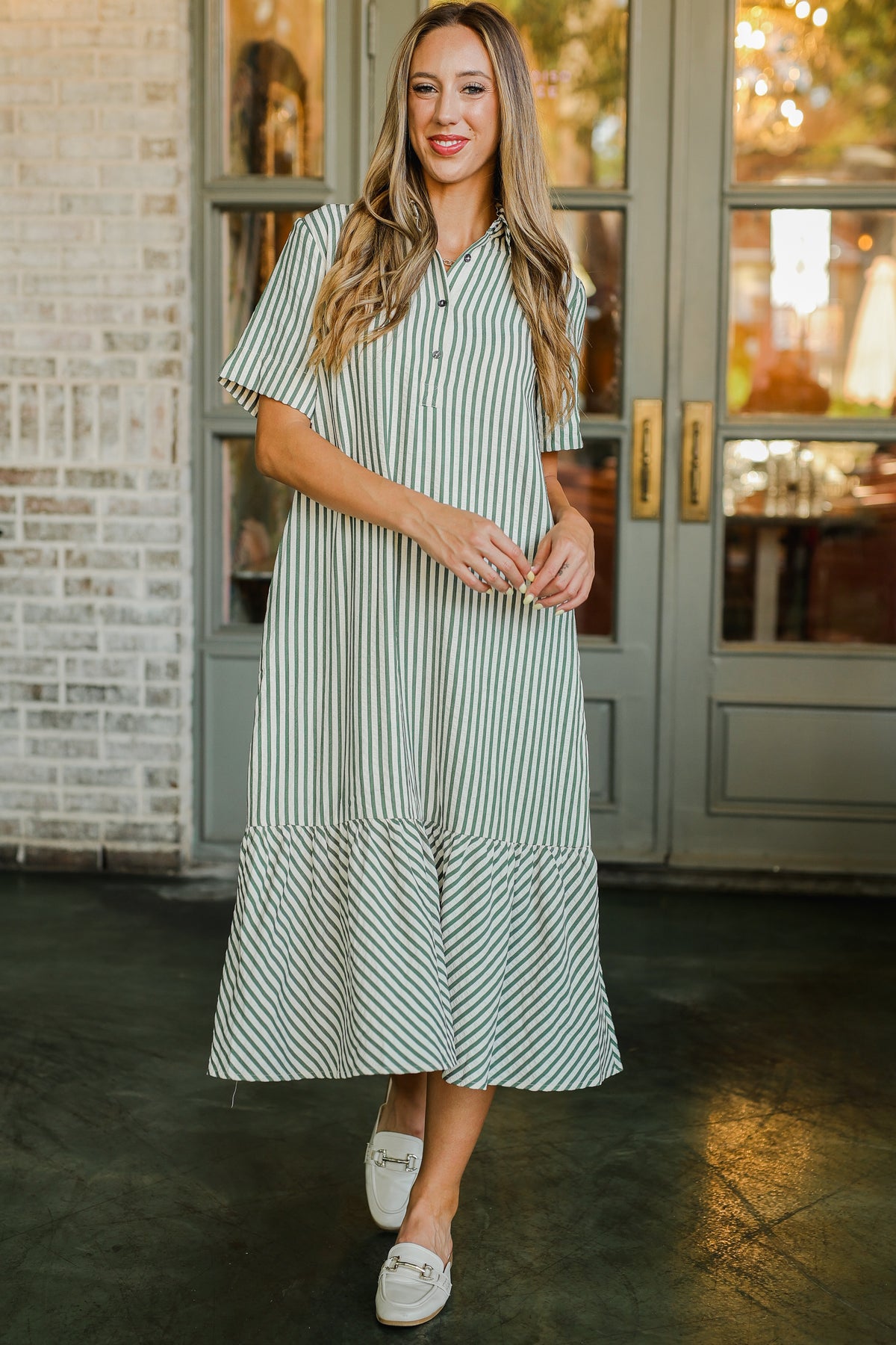 Woman wearing a green and white striped dress standing in front of a door.