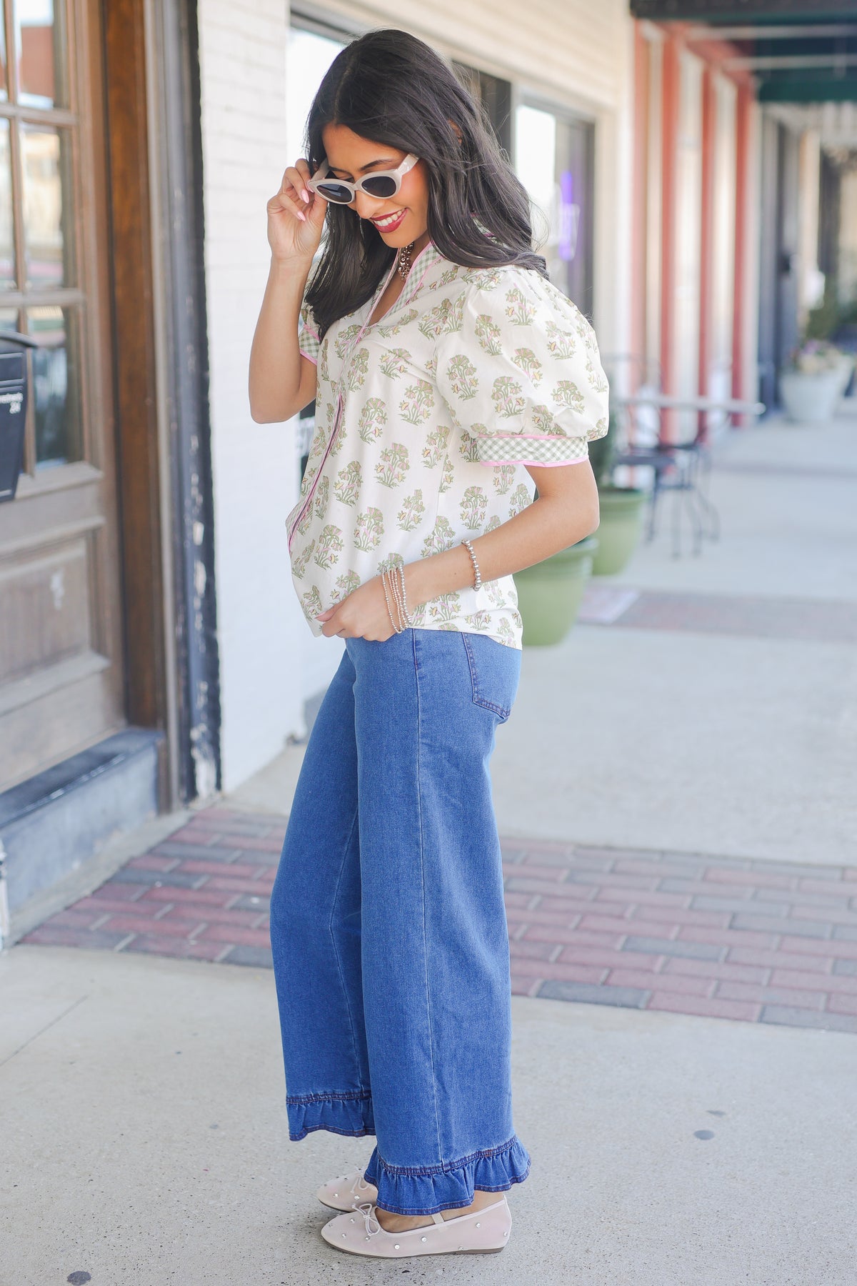 Woman wearing a floral blouse and blue jeans standing on a sidewalk.