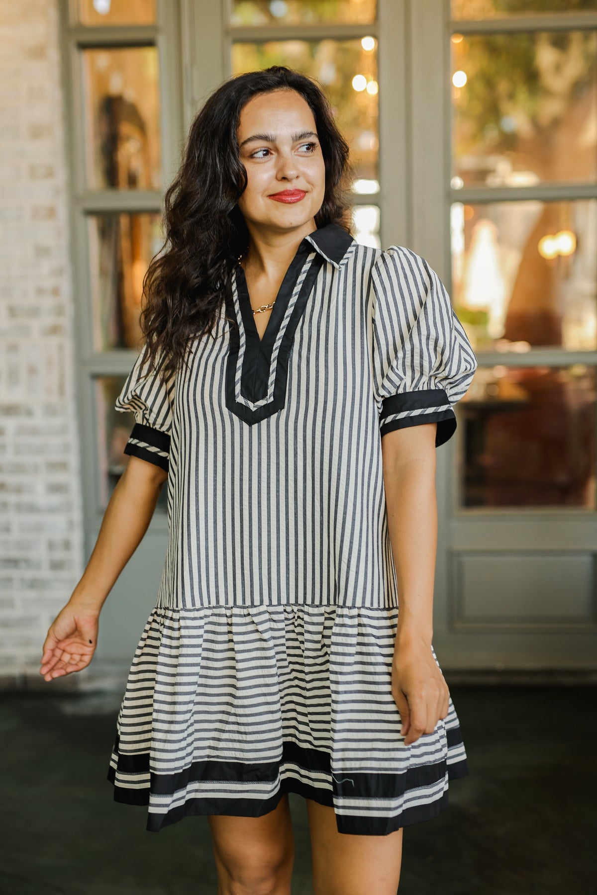 Woman wearing a black and white striped dress with a V-neckline in front of a window.