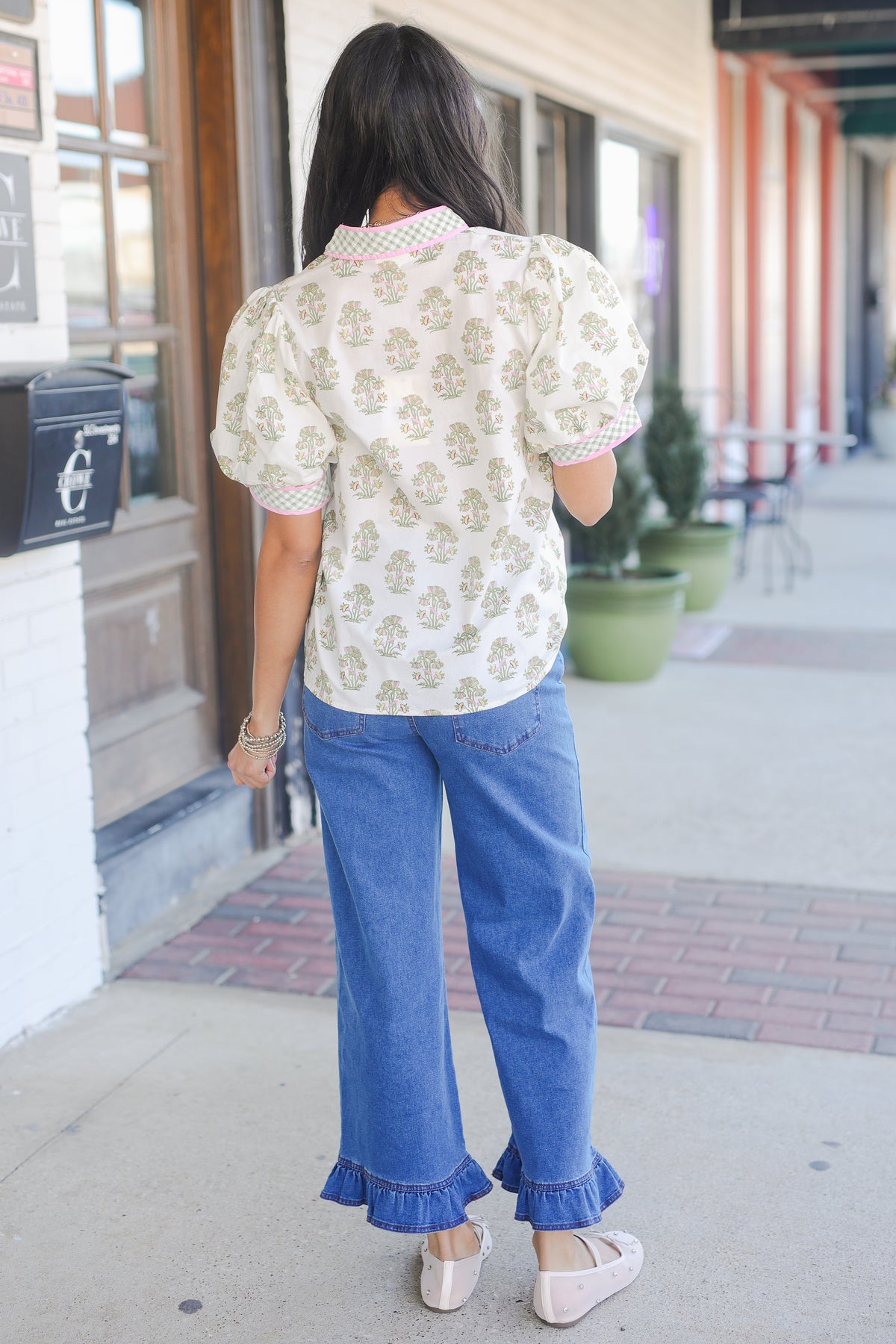 Woman wearing a floral blouse and blue jeans on a sidewalk.