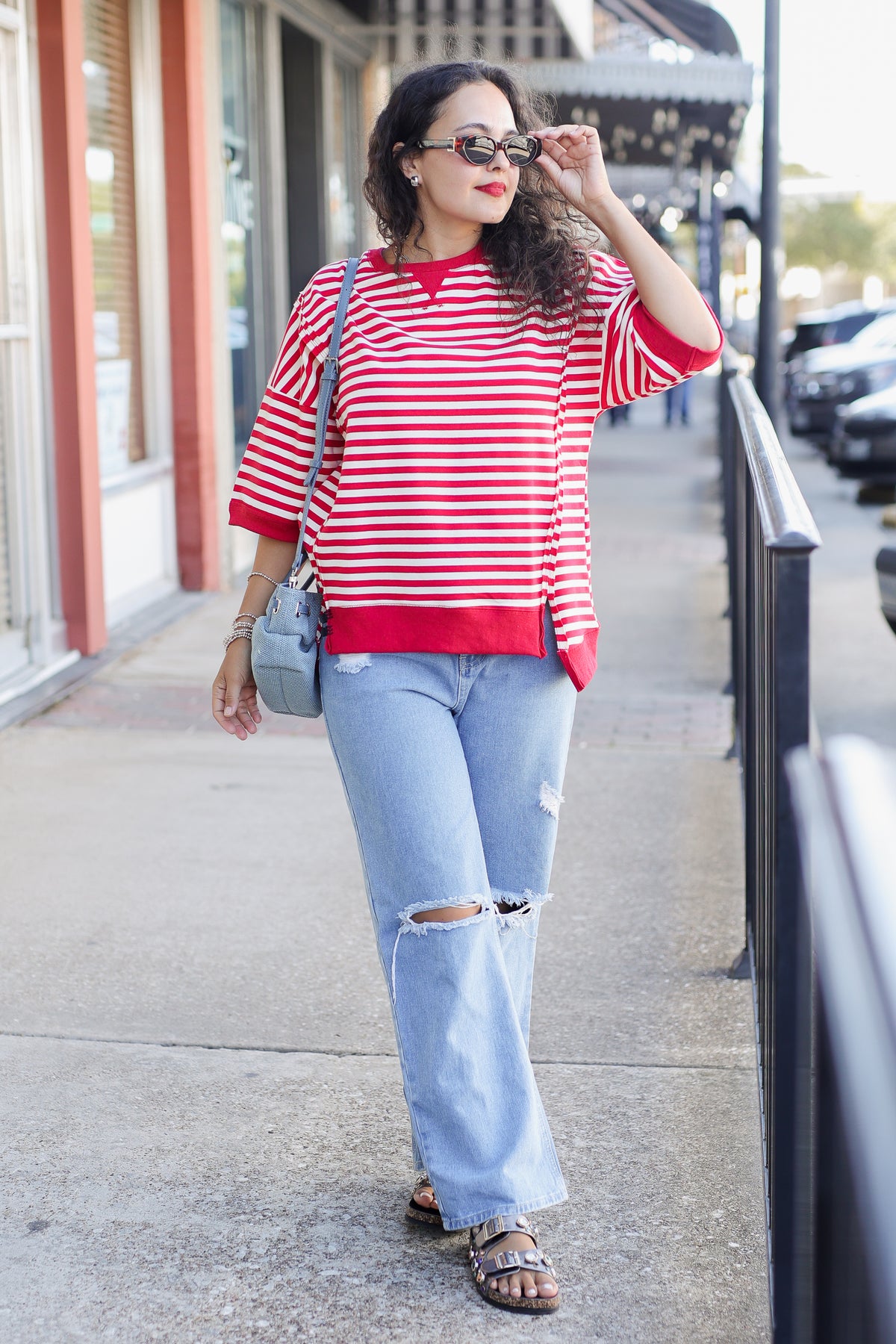Woman wearing a red and white striped shirt and ripped jeans on a sidewalk.