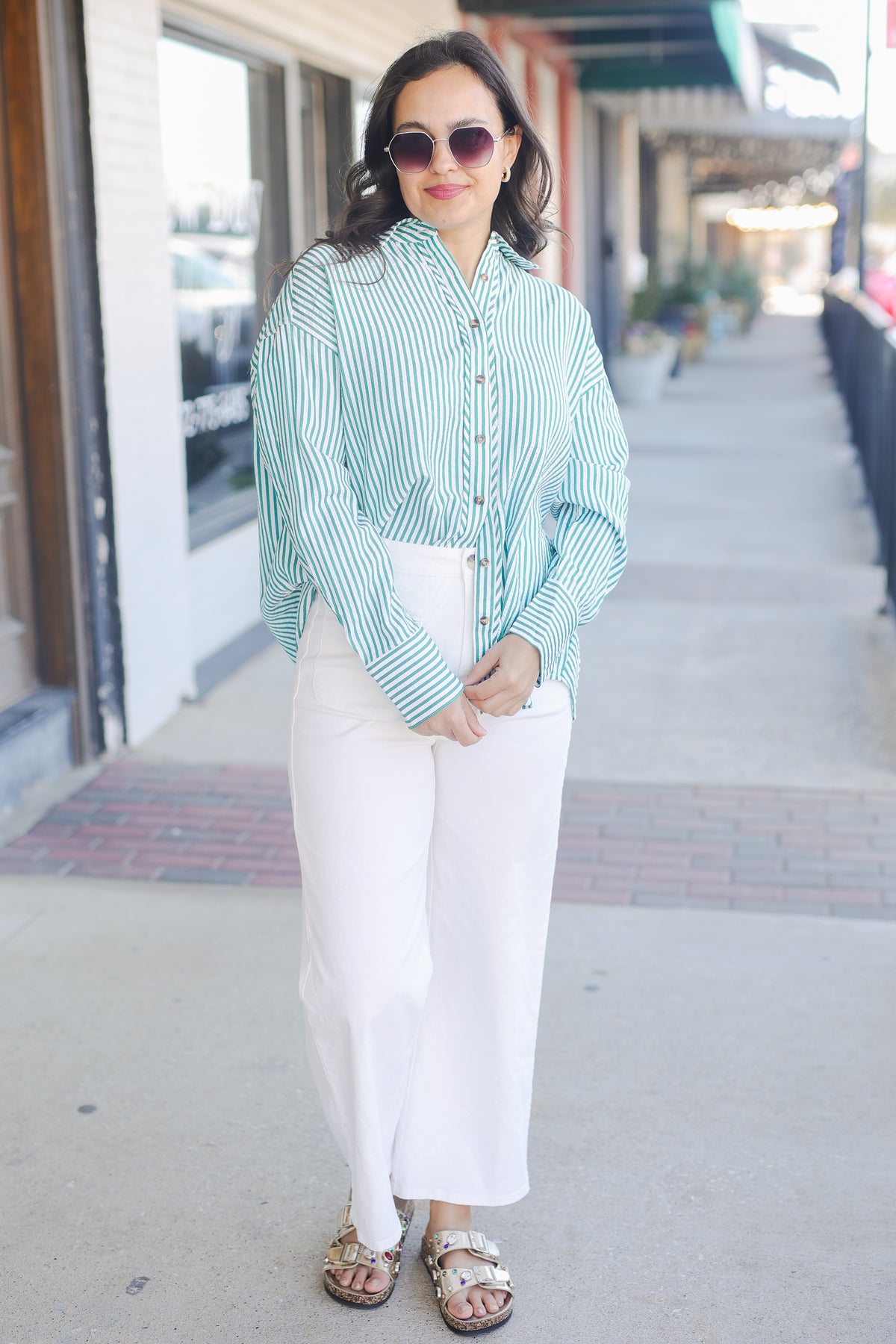 Woman wearing a green striped shirt and white pants on a city street.