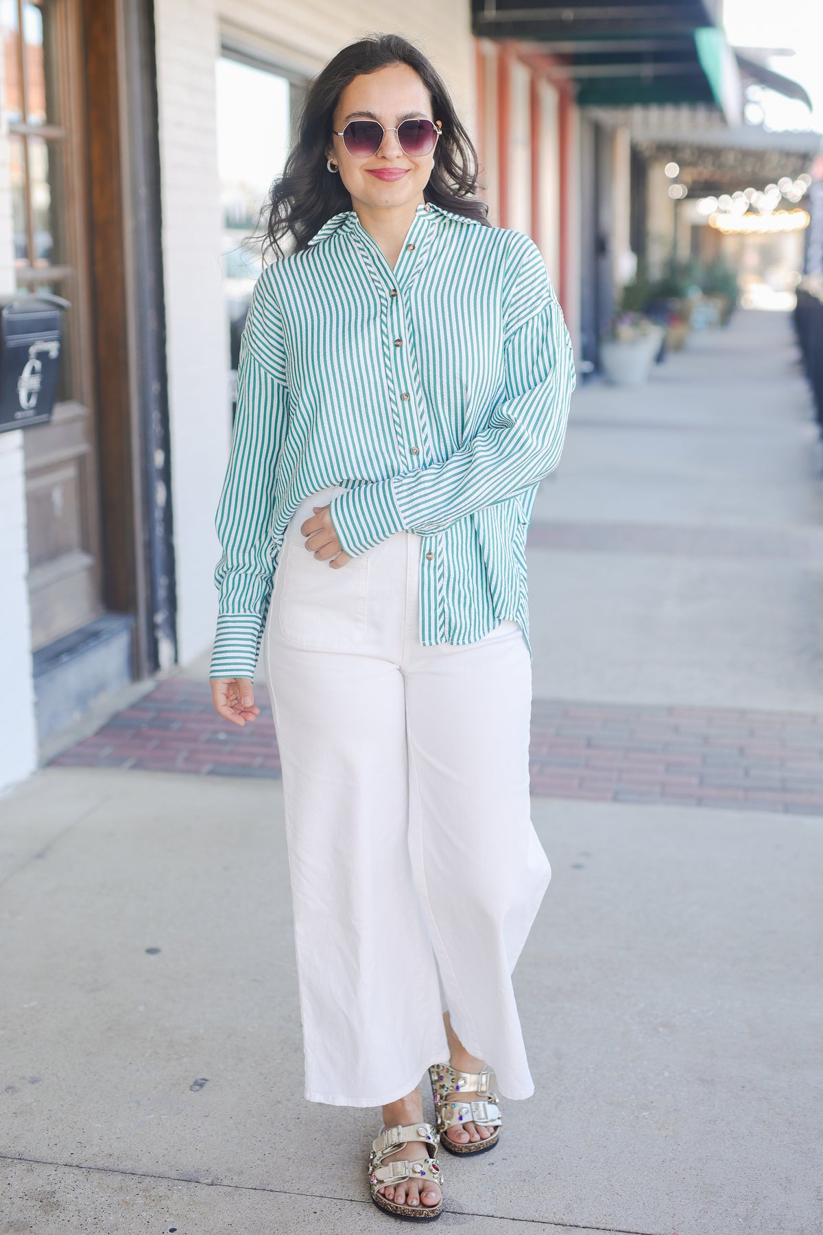 Woman wearing a green and white striped shirt and white pants on a sidewalk.