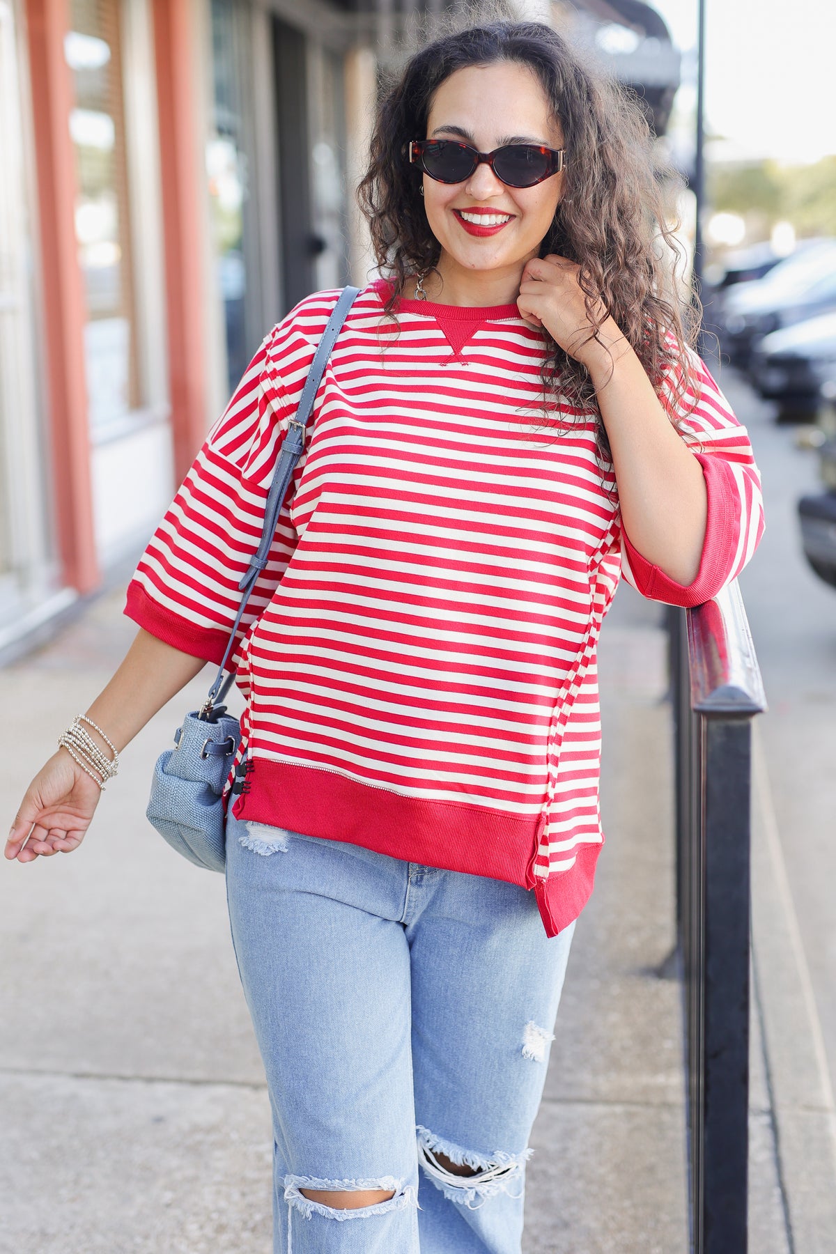 Woman wearing a red and white striped shirt and ripped jeans on a city street.